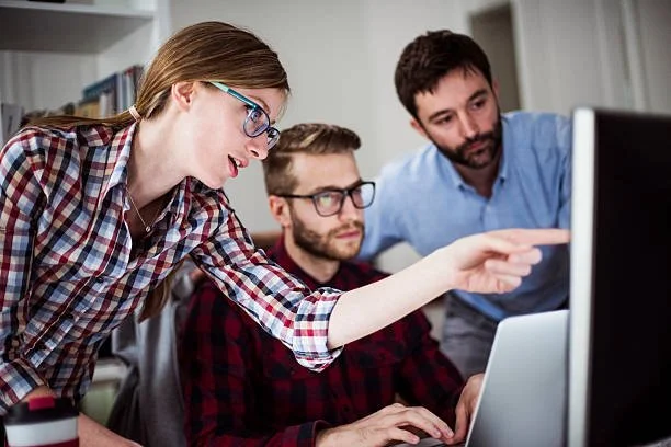 Three people working together at a computer in an office