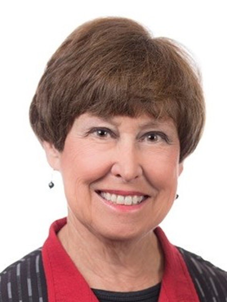 Close-up portrait of a smiling woman with short brown hair, wearing a black and red jacket and earrings against a plain white background.