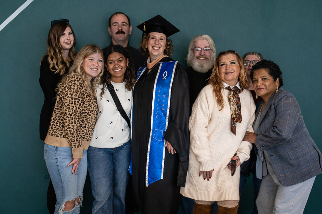 Group of nine people, including a woman in a graduation gown and cap, smiling and posing for a photo.