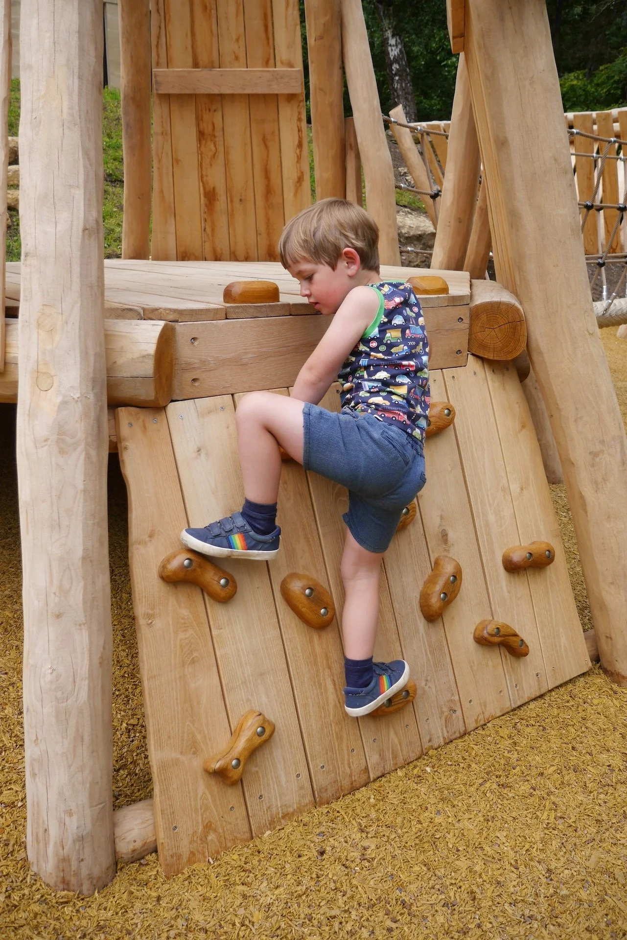 A young boy climbing a wooden rock wall on a playground structure.
