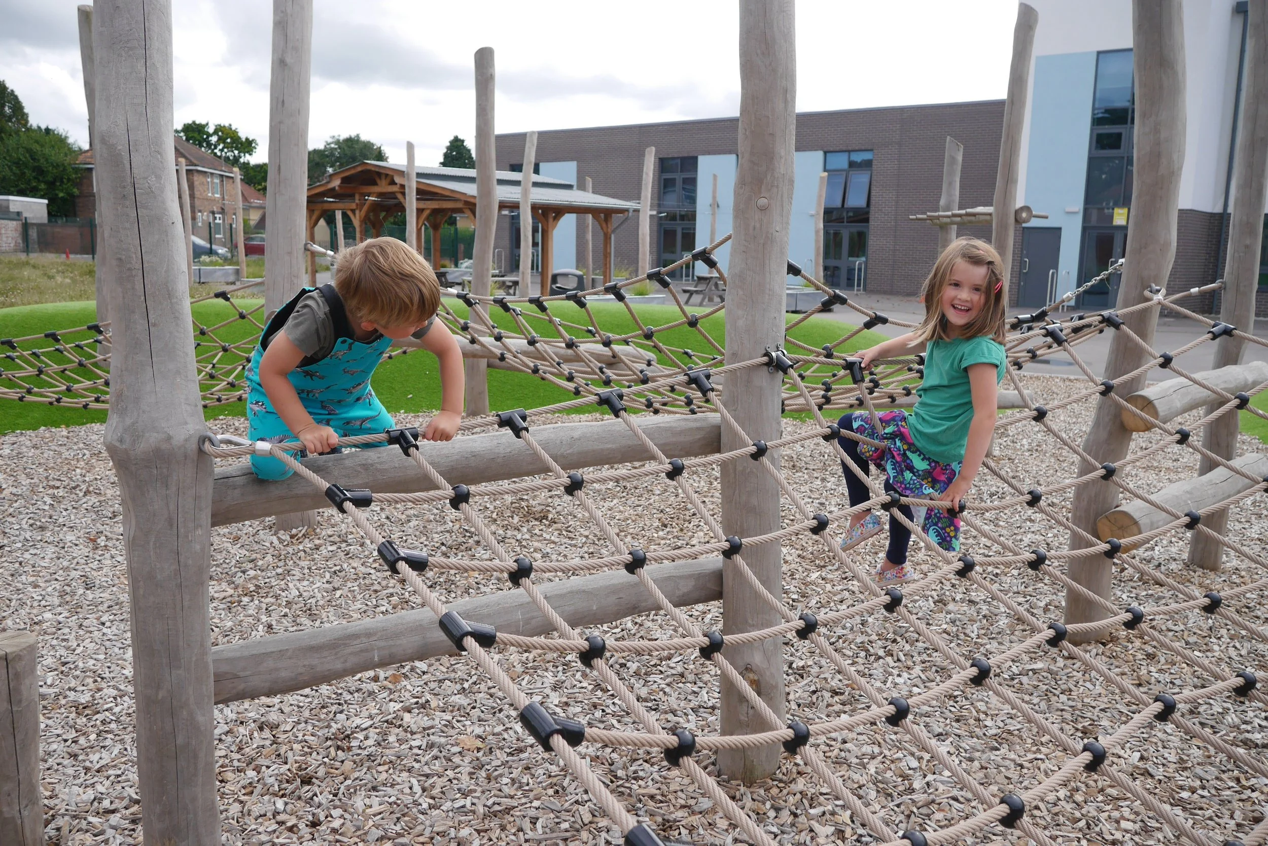 Two kids playing on a rope playground at a park.