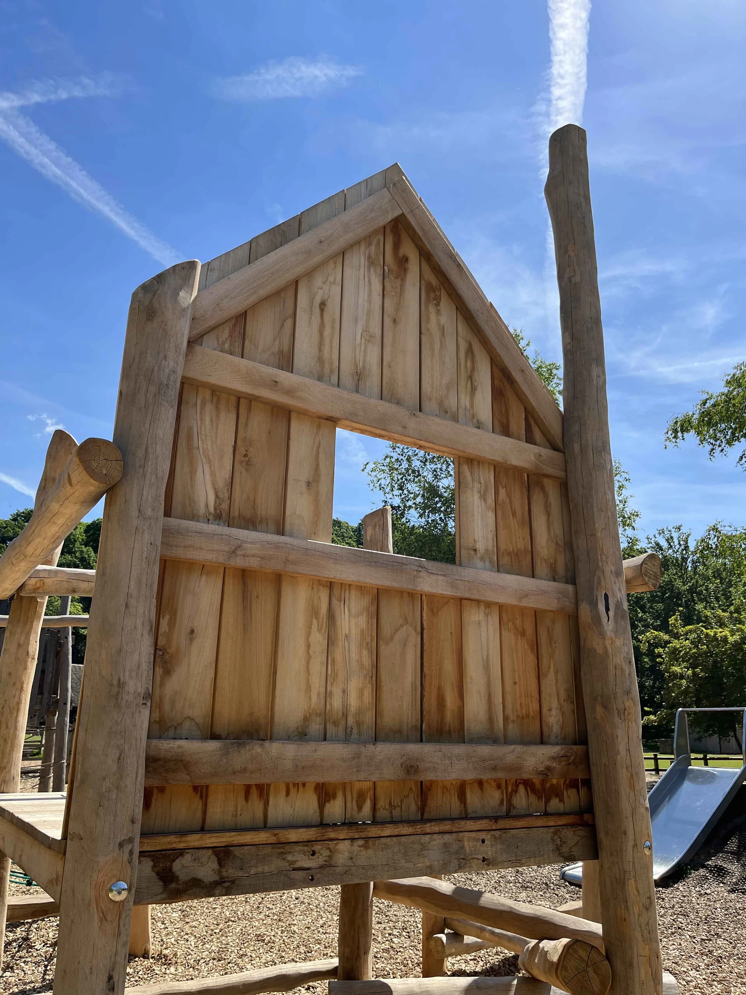 Wooden playground structure with a clear blue sky and some trees in the background.