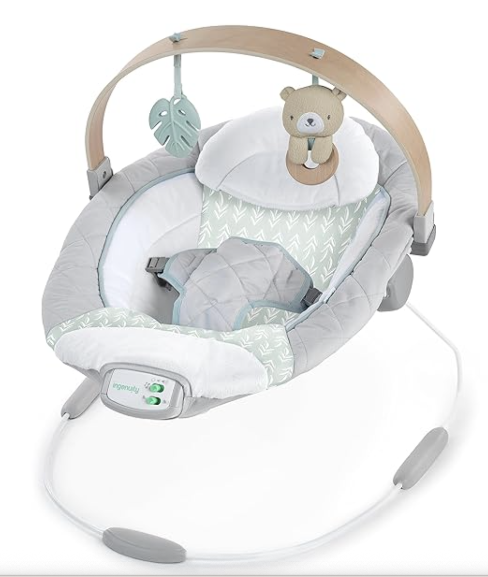 An infant swing featuring a plush teddy bear and a leaf-shaped hanging toy, with a padded seat and control buttons on the front.