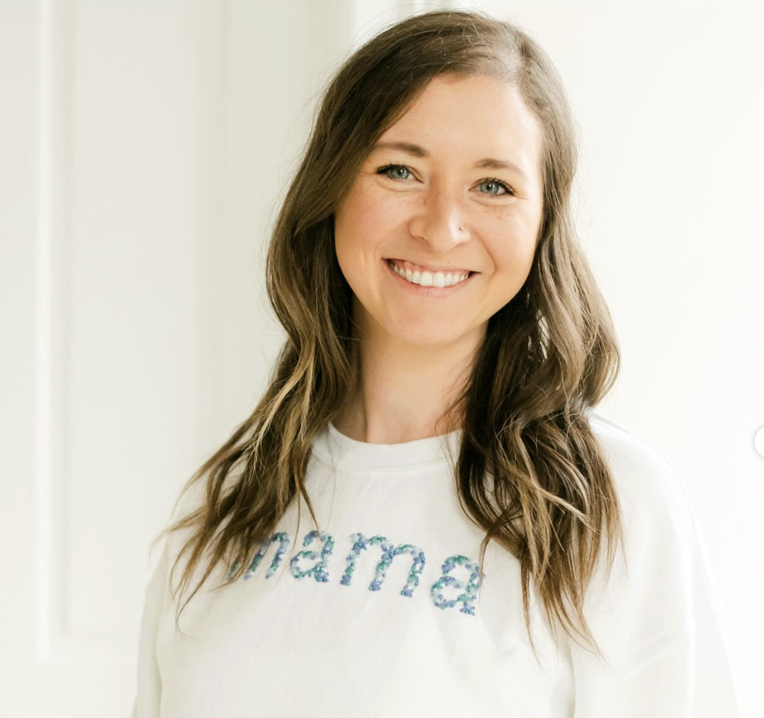 A young woman with wavy brown hair and blue eyes smiling, wearing a white shirt with the word 'Beautiful' written in blue.