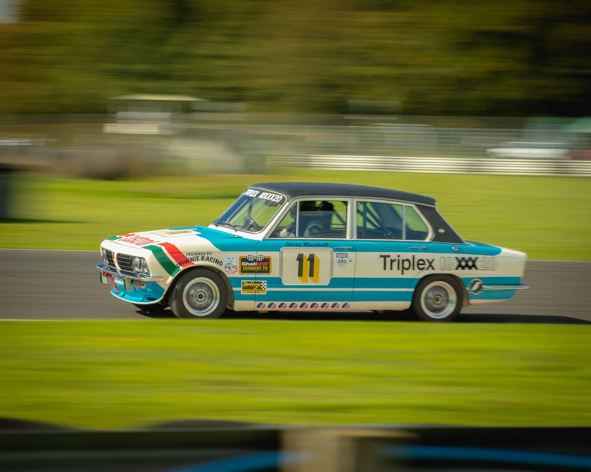 A classic race car with the number 11, colorful racing stripes, and various sponsor decals racing on a track with a blurred background indicating high speed.