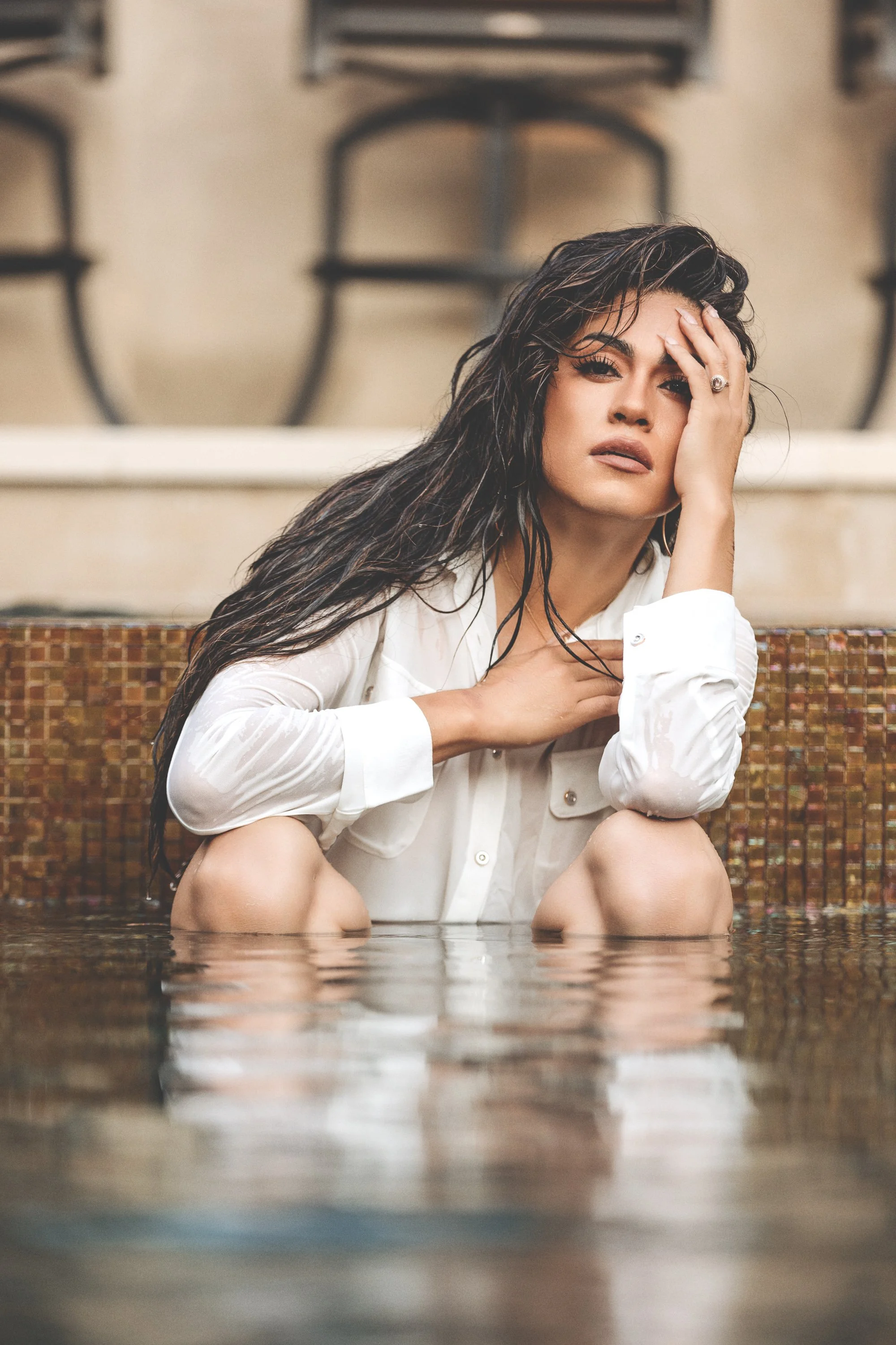 Luxury swimsuit portrait of a woman with wet hair wearing a white shirt while sitting in a resort-style pool, photographed by rgmphotography in Dallas-Fort Worth, Texas.