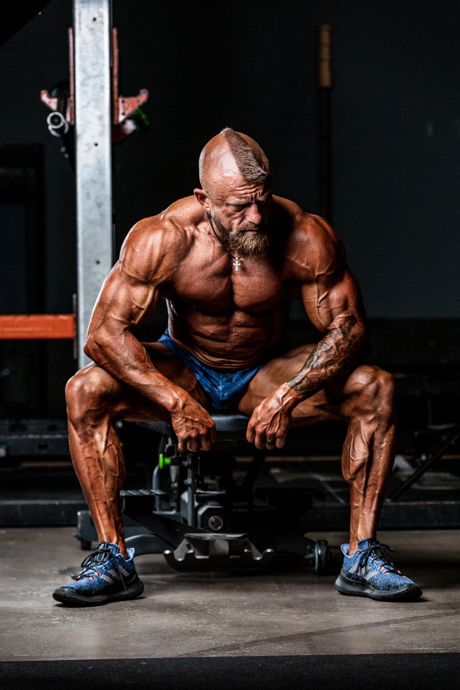 Male bodybuilder sitting on gym bench post-set in dramatic lighting, Destination Dallas shoot by rgmphotography
