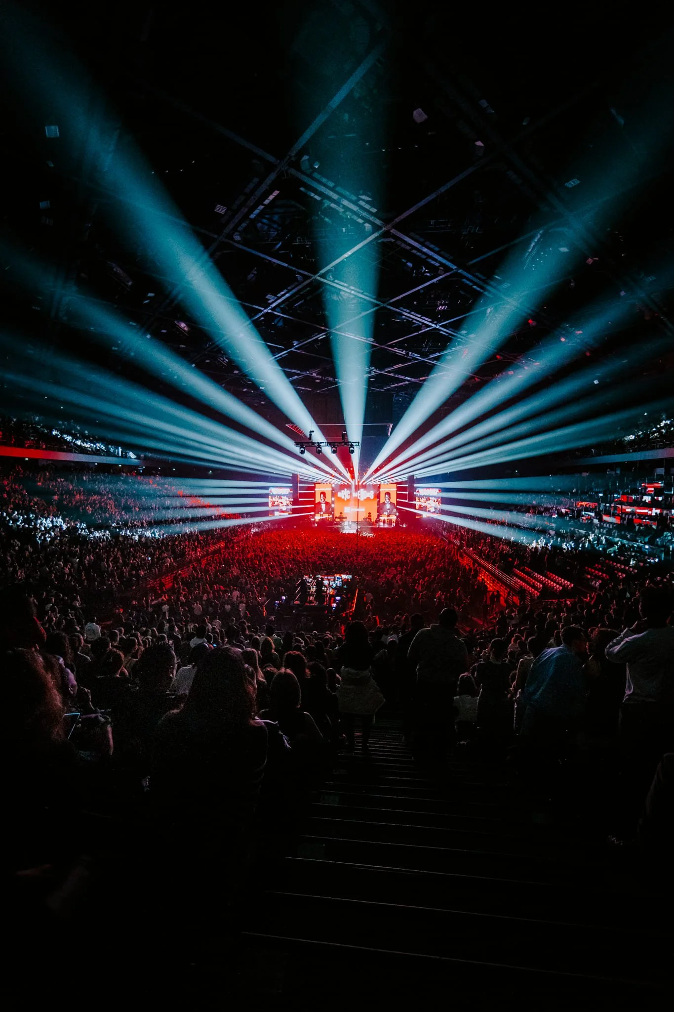 Intérieur d'une salle de concert ou d'un événement avec un public nombreux, confettis, et un spectacle avec des lumières et écrans lumineux à l'avant.
