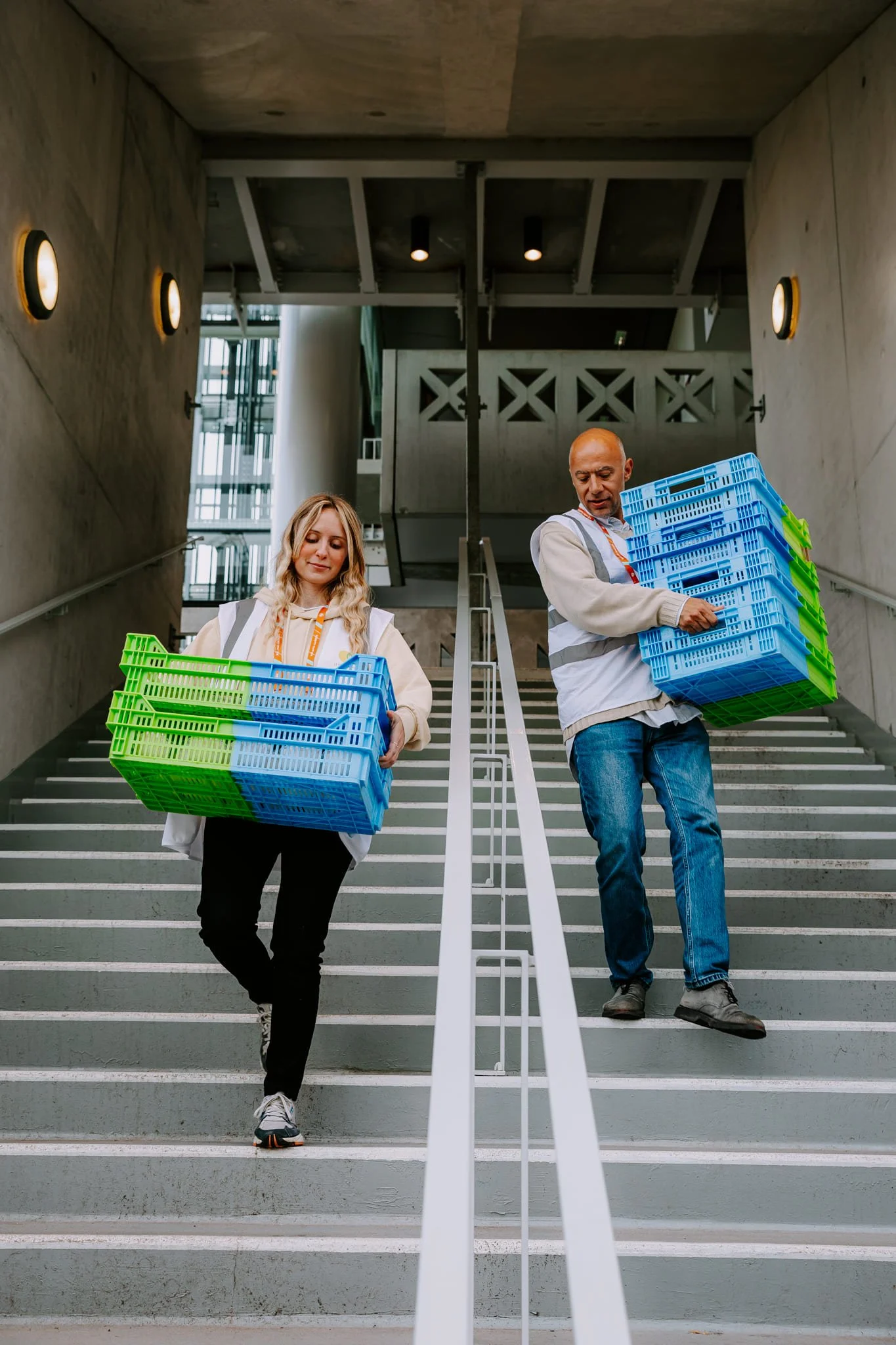 Reportage photo auprès de l'association solidaire et anti-gaspi Le Chainon Manquant. Deux bénévoles descendent les escaliers de Rolland Garros en portant des caisses de nourriture récupérées, destinées à être distribuées.