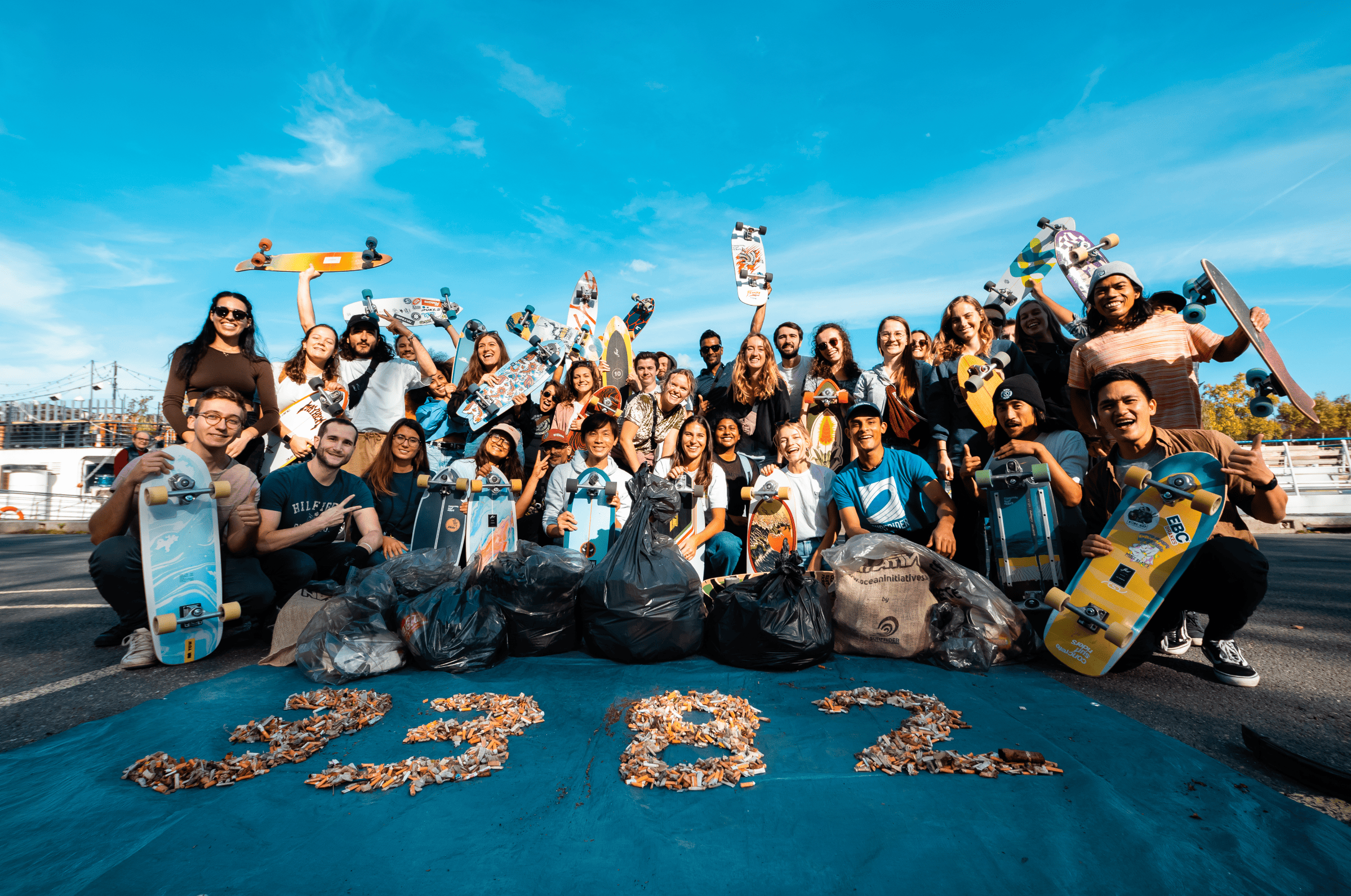 Groupe de bénévoles Surfrider posant avec des skateboards, des sacs de déchets, et le chiffre 3382 écrit en mégots de cigarette, lors d'une opération de nettoyage et de sensibilisation à l'environnement sur les quais de Seine à Paris.