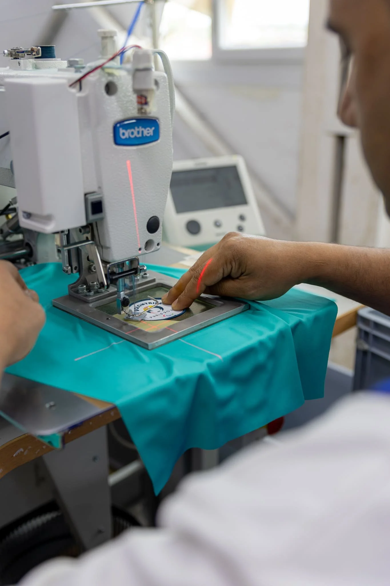 Reportage photo dans un atelier textile marseillais. On y voit un homme coudre un écusson "Paris 2024" à la machine.