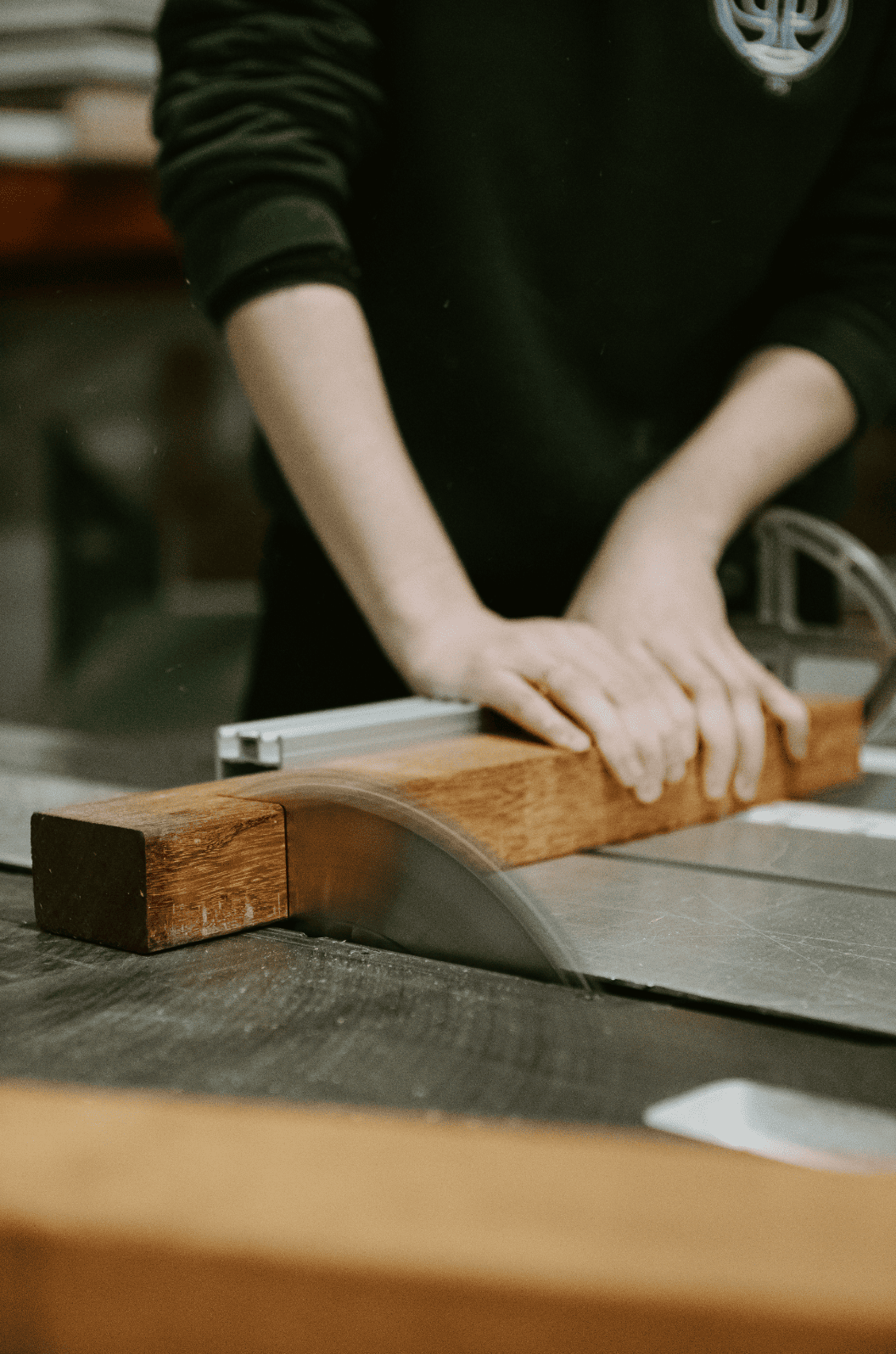 Une personne coupe une pièce de bois avec une scie à table dans un atelier de menuiserie.