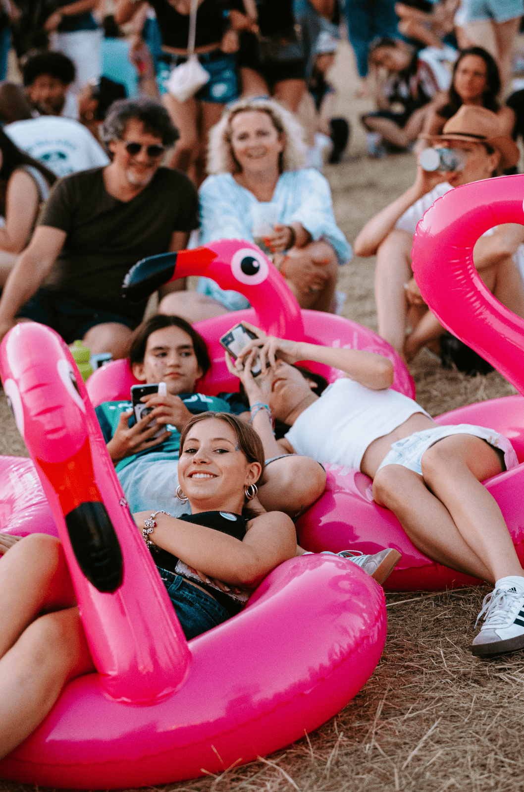 Groupe de jeunes adultes relaxant sur des matelas gonflables en forme de flamant rose lors d'un événement en plein air, certains utilisant leur téléphone
