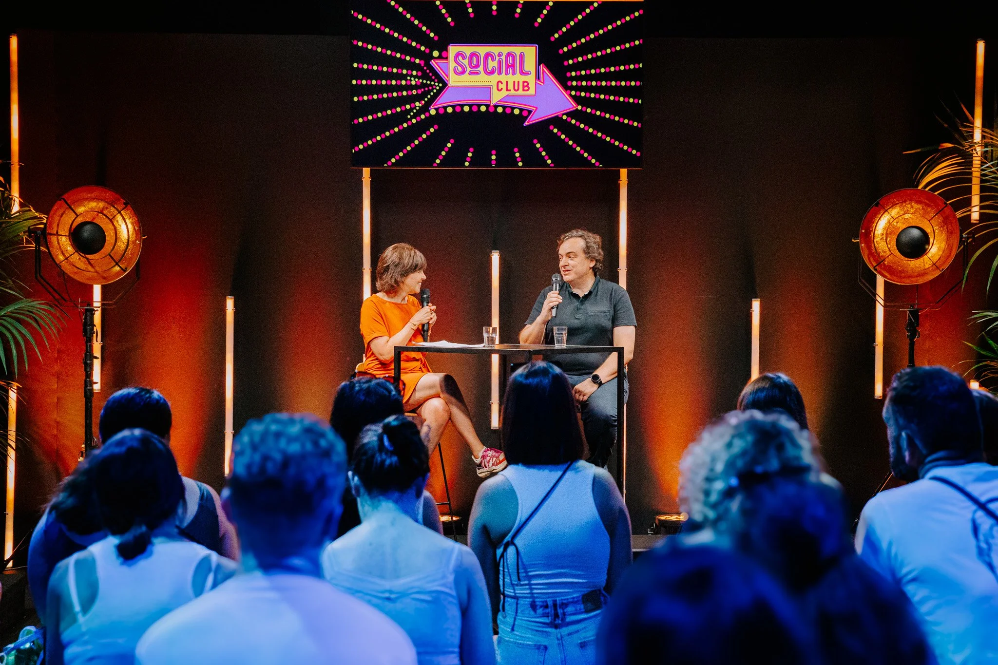 Photo prise au Social Club de Solidays. Une animatrice et un scientifique échangent face au public lors d'une conférence, avec un écran indiquant 'Social Club' en arrière-plan.