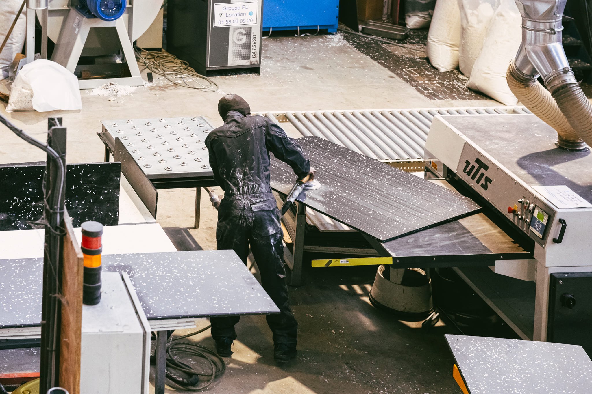 Reportage dans l'usine francilienne "Le Pavé" qui fabrique un matériau de construction à partir de déchets plastiques. Un ouvrier shooté d'en haut utilise une machine pour polir le matériau recyclé.