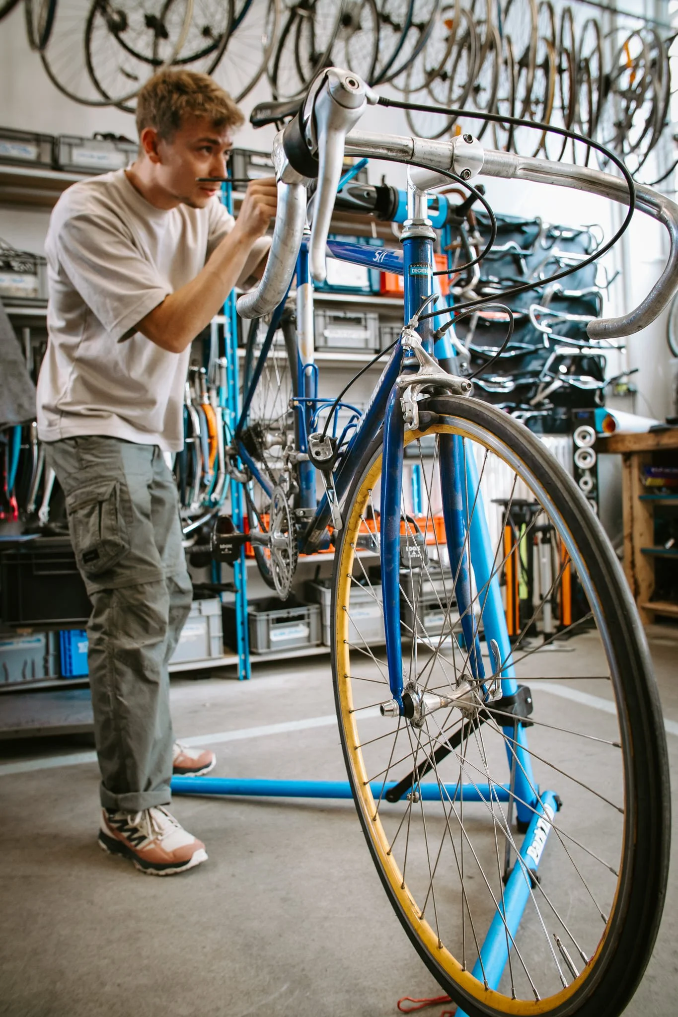 Photo prise dans l'atelier de réparation de vélo de la Recyclerie Sportive. Un homme travaille sur un vélo, entouré d'outils et de roues suspendues au mur.