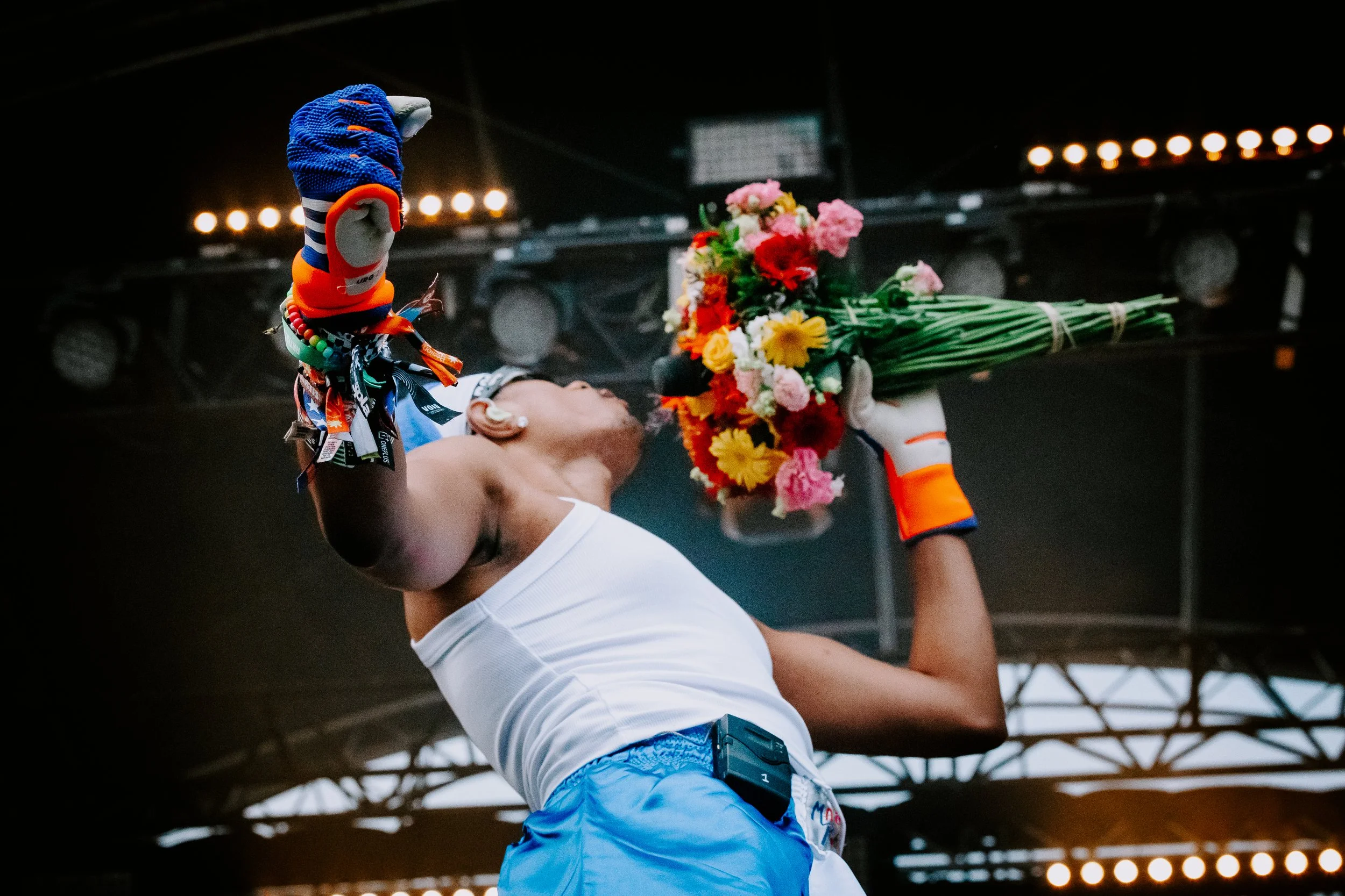 Véloceleuse féminine portant un maillot blanc, des gants à rayures orange et blanc, tenant un bouquet de fleurs colorées lors d'une cérémonie de victoire.