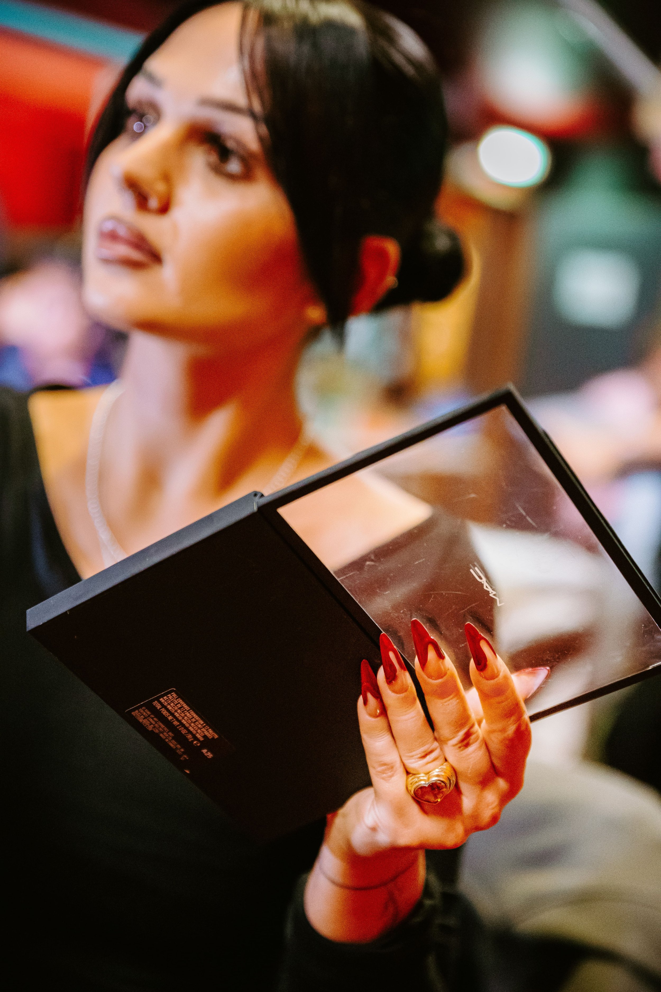 Une maquilleuse avec des ongles longs et rouges, tient une palette de maquillage MAC. On devine qu'elle est en train de maquiller quelqu'un.