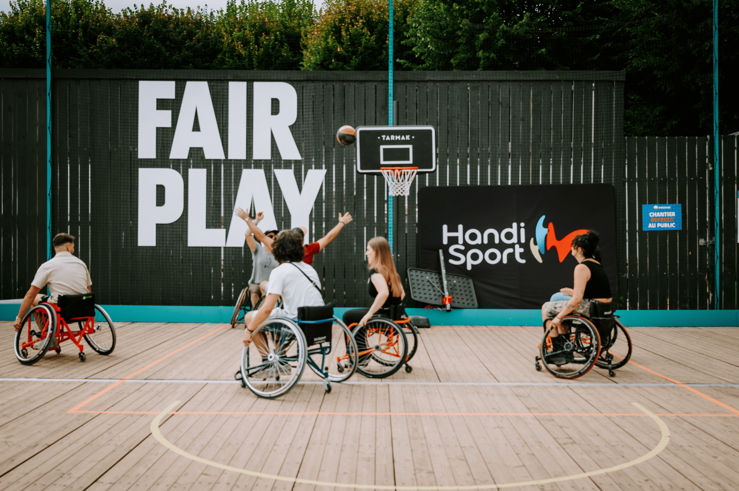 Photo prise à Rock en Seine. On y voit un groupe de personnes en fauteuil roulant jouant au basket-ball sur un terrain en bois avec un panneau "Fair Play" en arrière-plan.