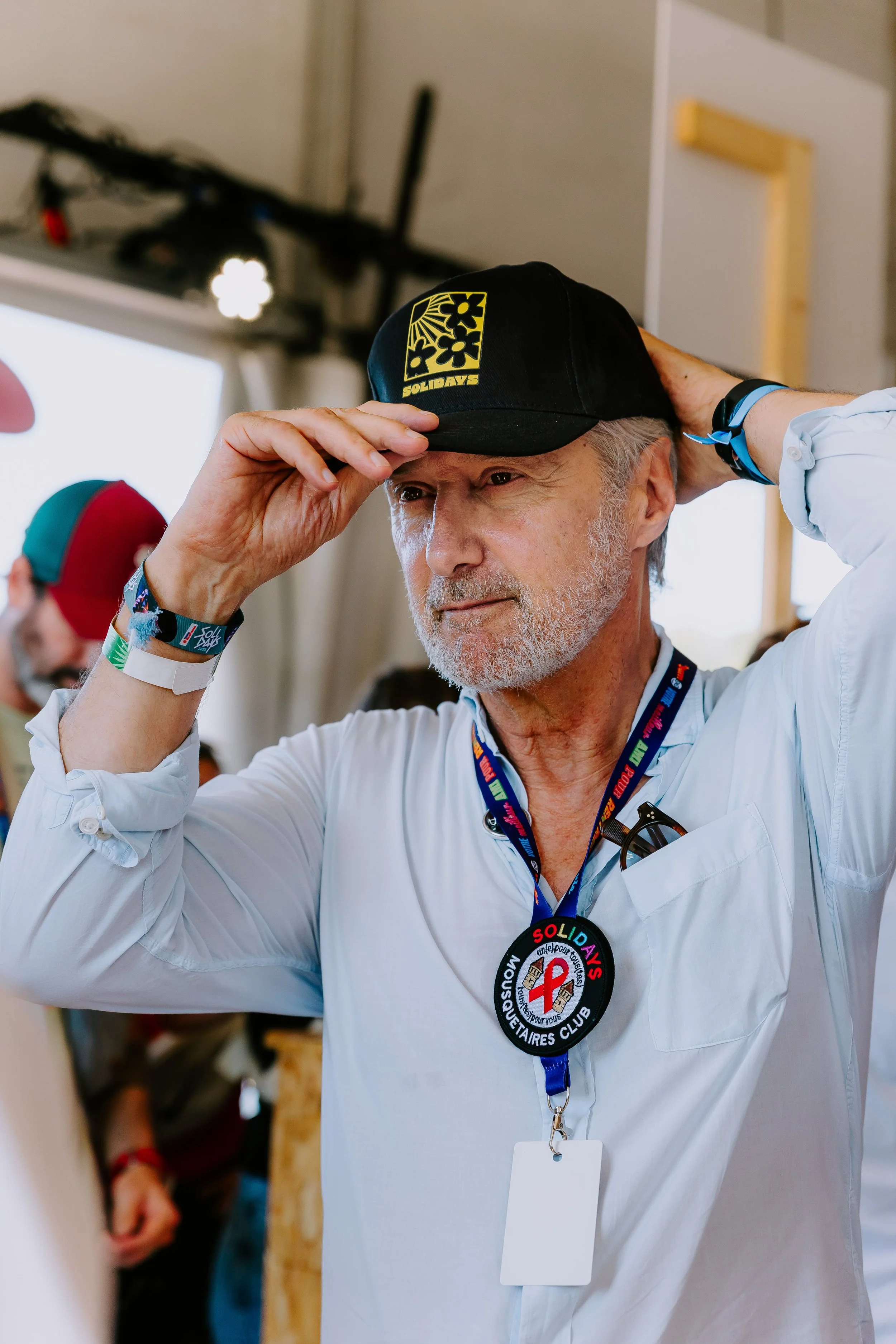 Antoine de Caunes, souriant, ajuste une casque noire Solidays. Il porte un écusson « Solidays Mousquetaire Club ».