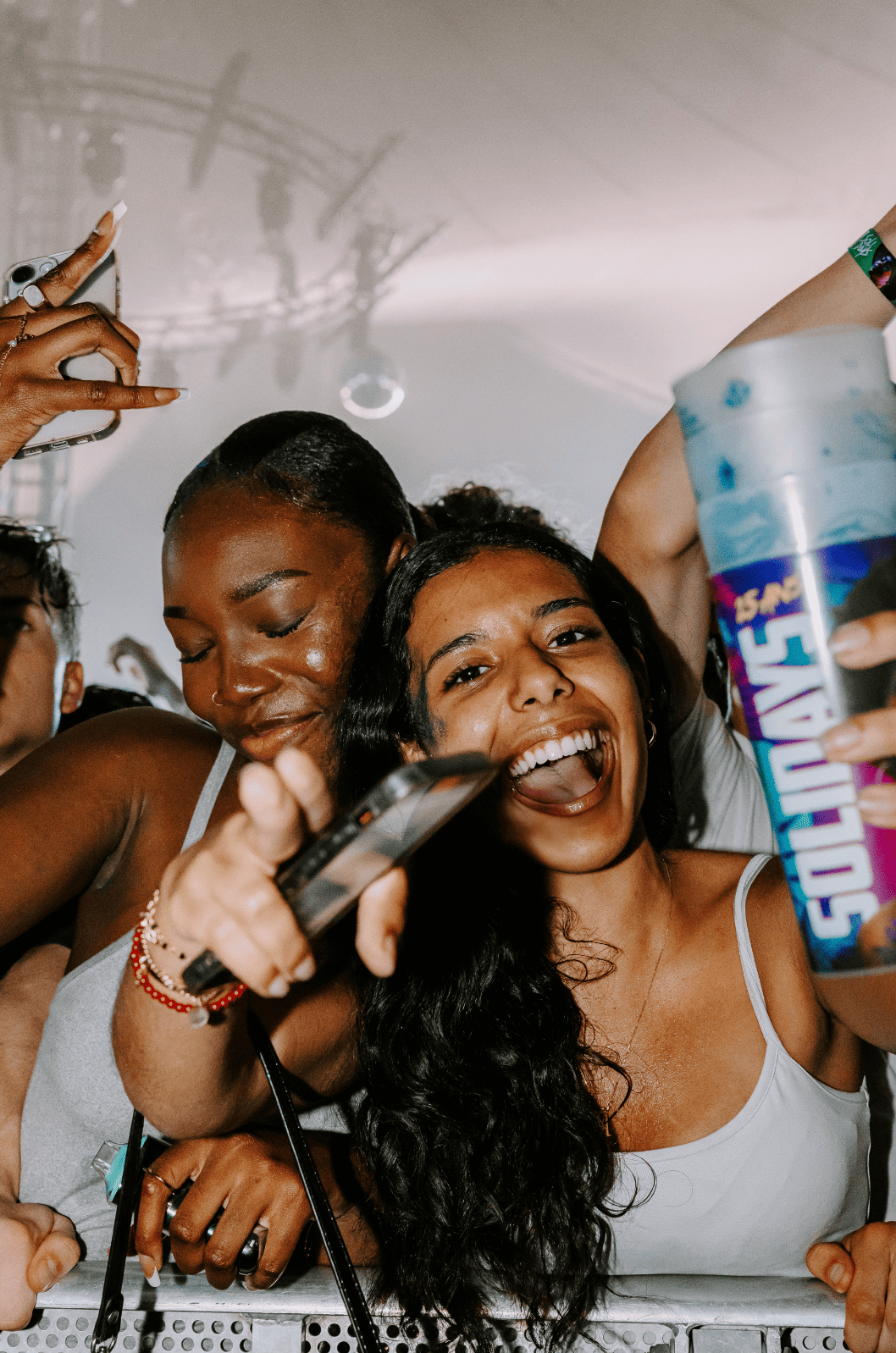 Deux femmes joyeuses faisant la fête, l'une tient une canette de Funtones, l'autre un téléphone portable, smiles et ambiance festive.