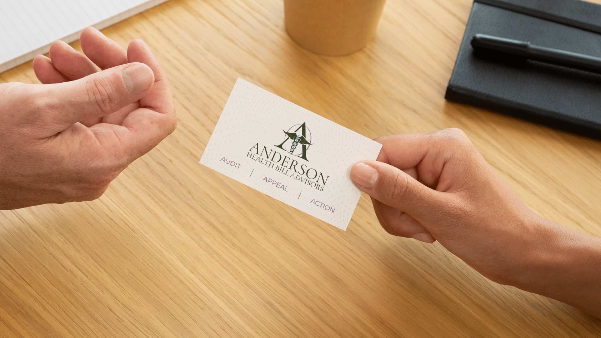 Two people exchanging a business card for Anderson Health Bill Advisers, with a wooden desk, notebook, and pen in the background.