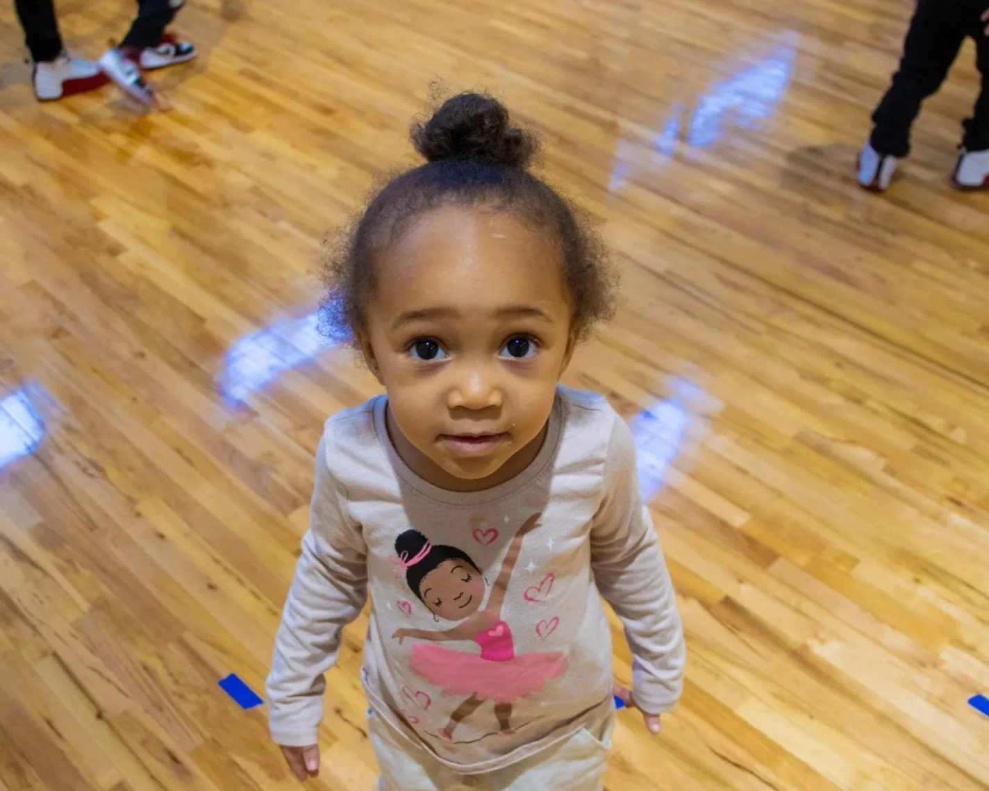 A  child wearing a ballerina shirt looking up at the camera