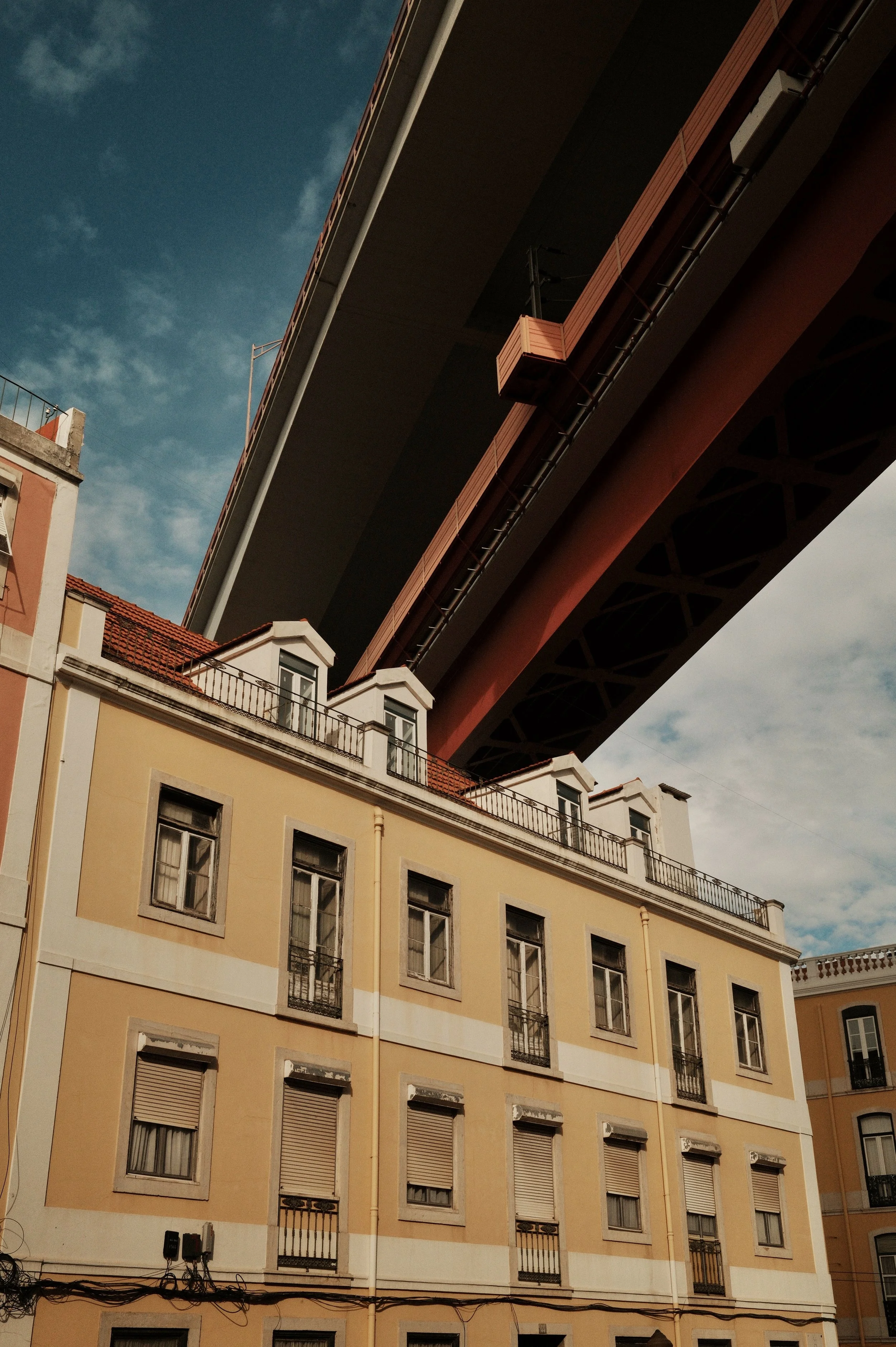 View of a large elevated highway or bridge structure over a historic yellow building with multiple windows and small balconies, with partly cloudy sky in the background.