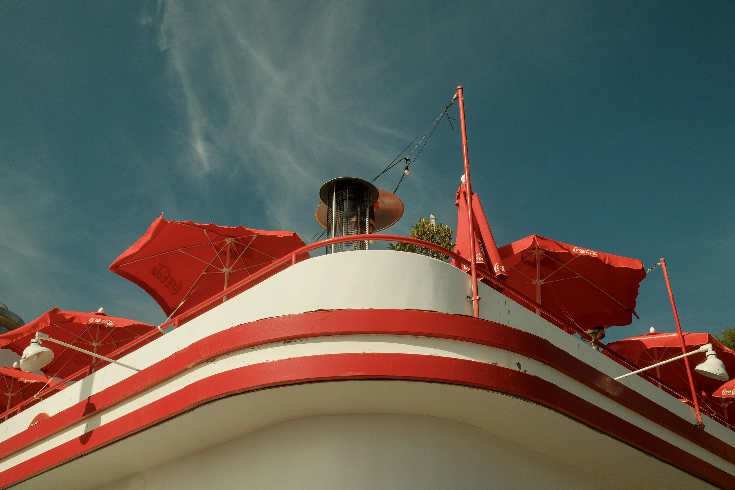 A white building with red accents and red umbrellas on the roof, under a clear blue sky.