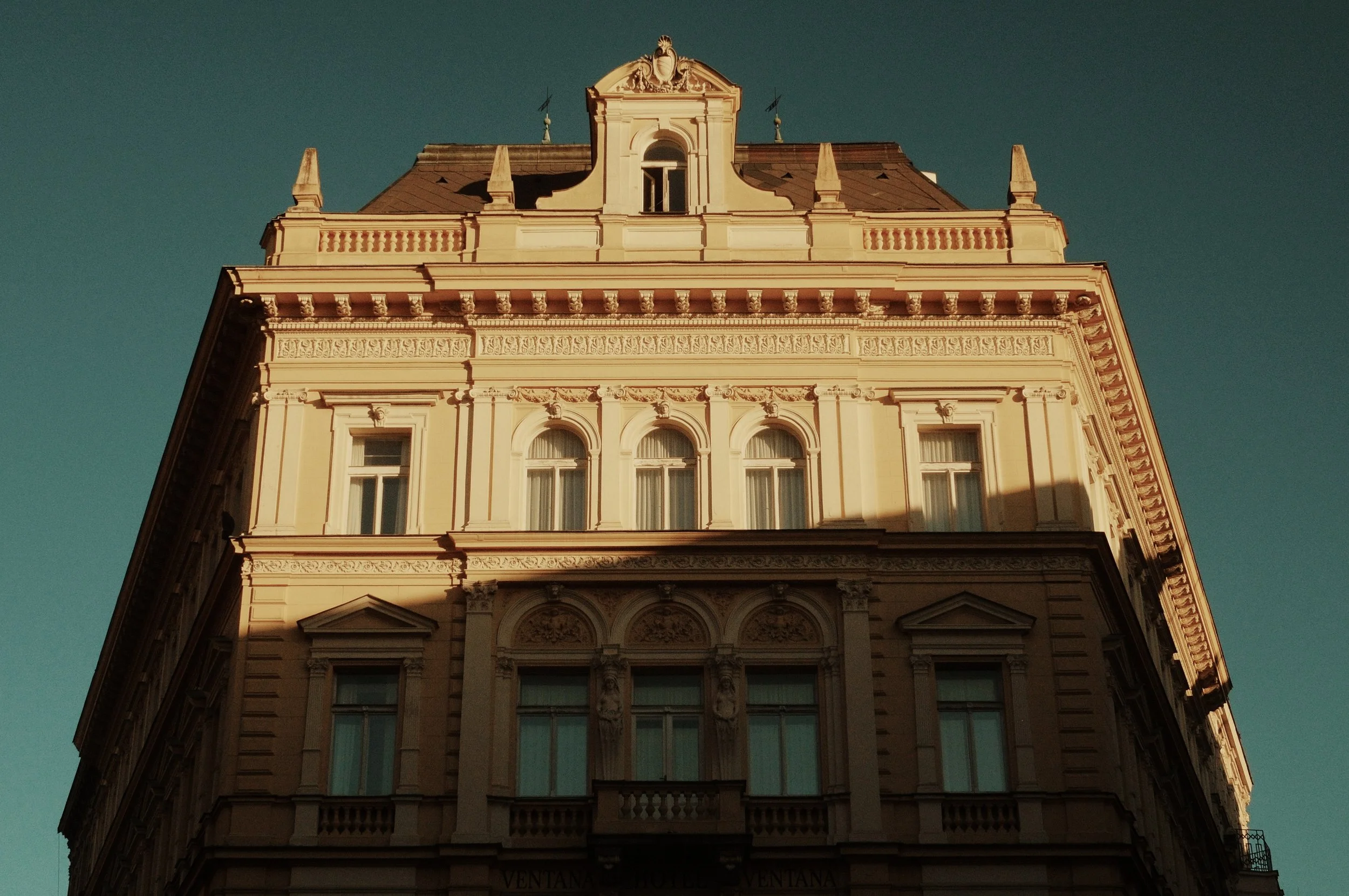 A close-up view of a historic, ornate building with classical architectural details, illuminated by sunlight, against a clear sky.