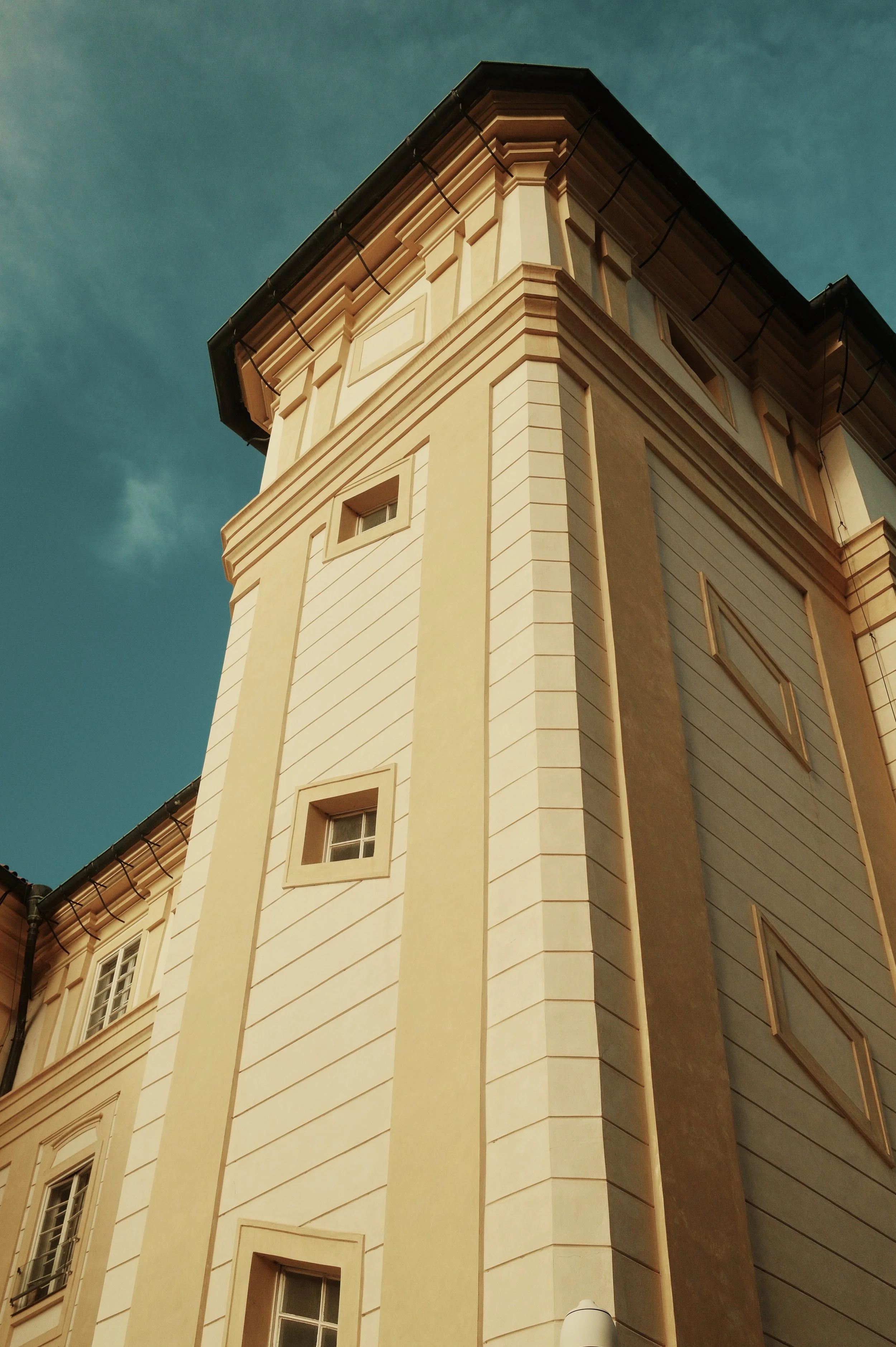 A tall beige building with multiple windows and decorative architectural details, viewed from below against a clear sky.