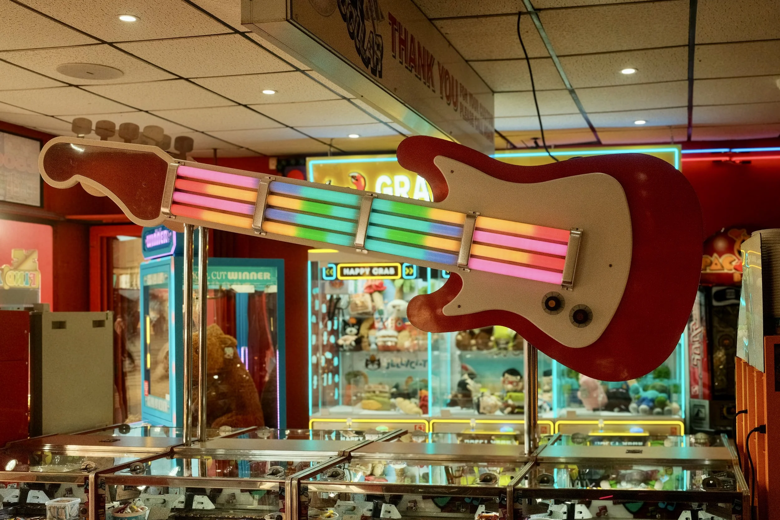 A colorful neon guitar arcade game in a game arcade with a background of arcade and claw machines.