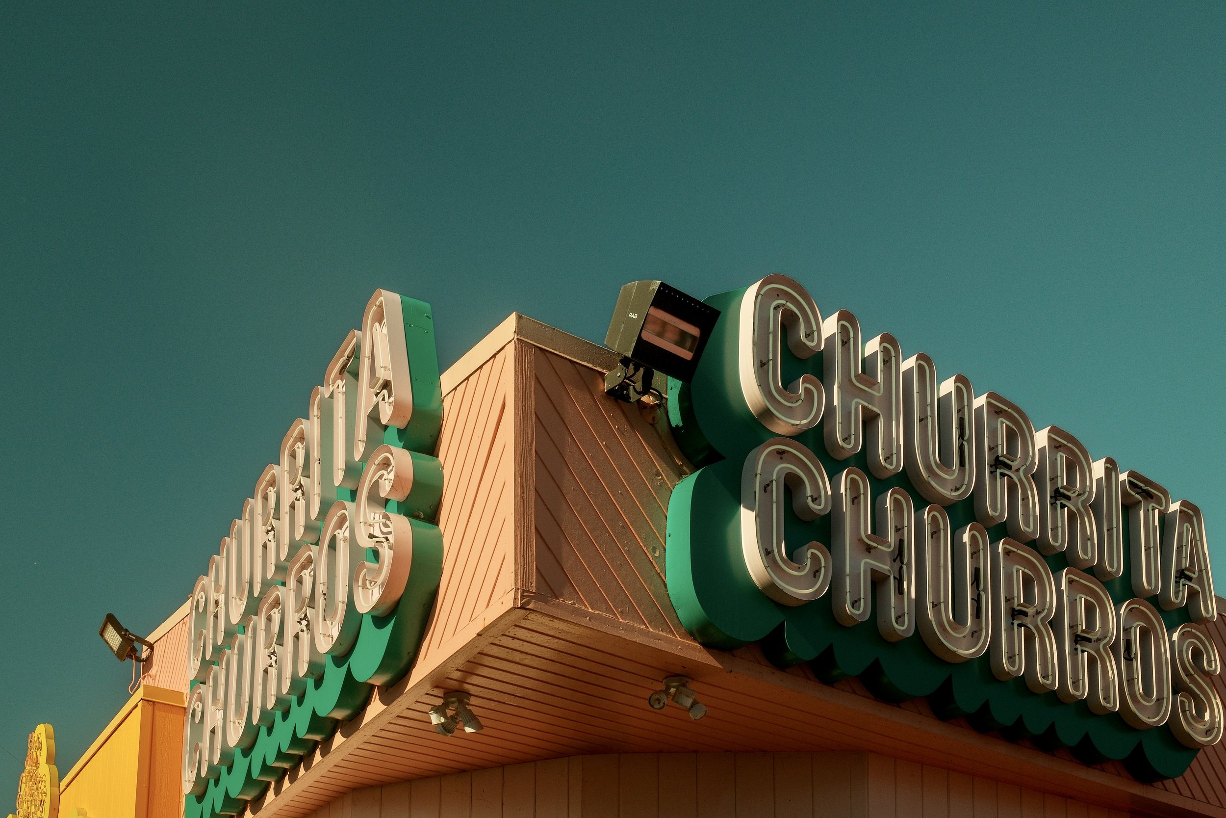 Close-up of colorful vintage sign reading "CHURRITOS" and "CHURRIA" against a clear sky.