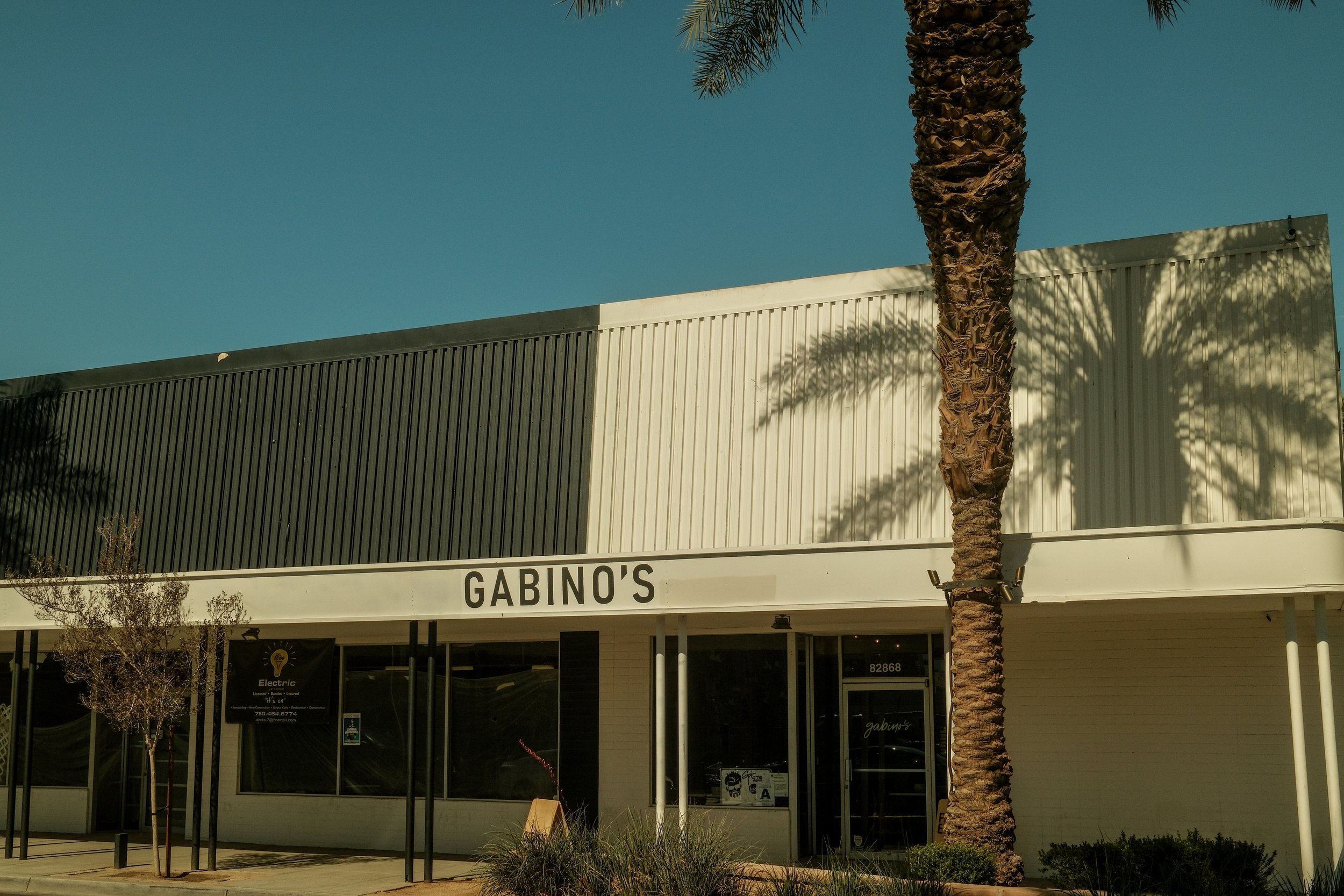 Exterior of Gabino's restaurant with a large palm tree in front, clear sky, and modern building facade.