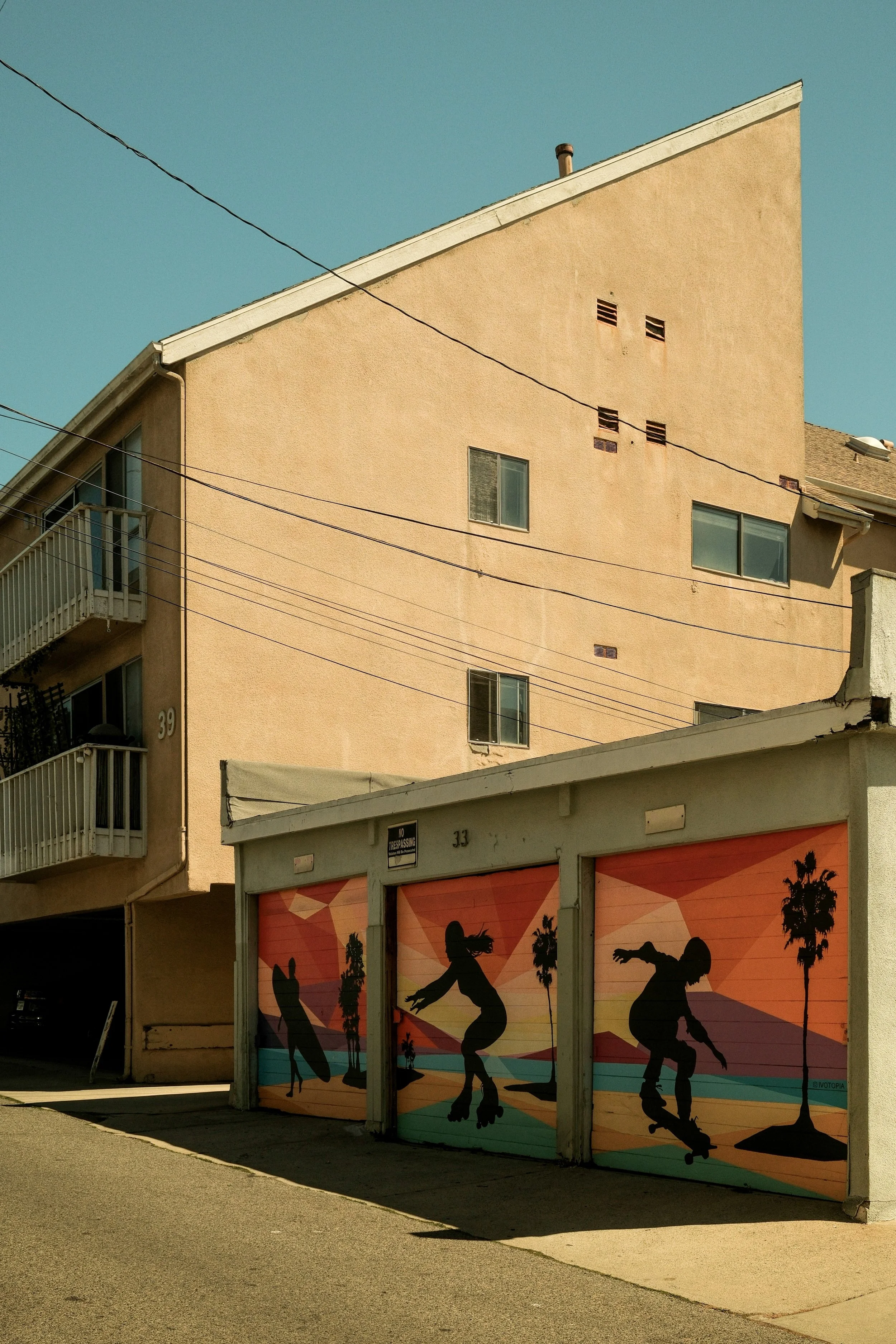 Garage doors with silhouettes of people skateboarding against a colorful sunset background and palm trees.