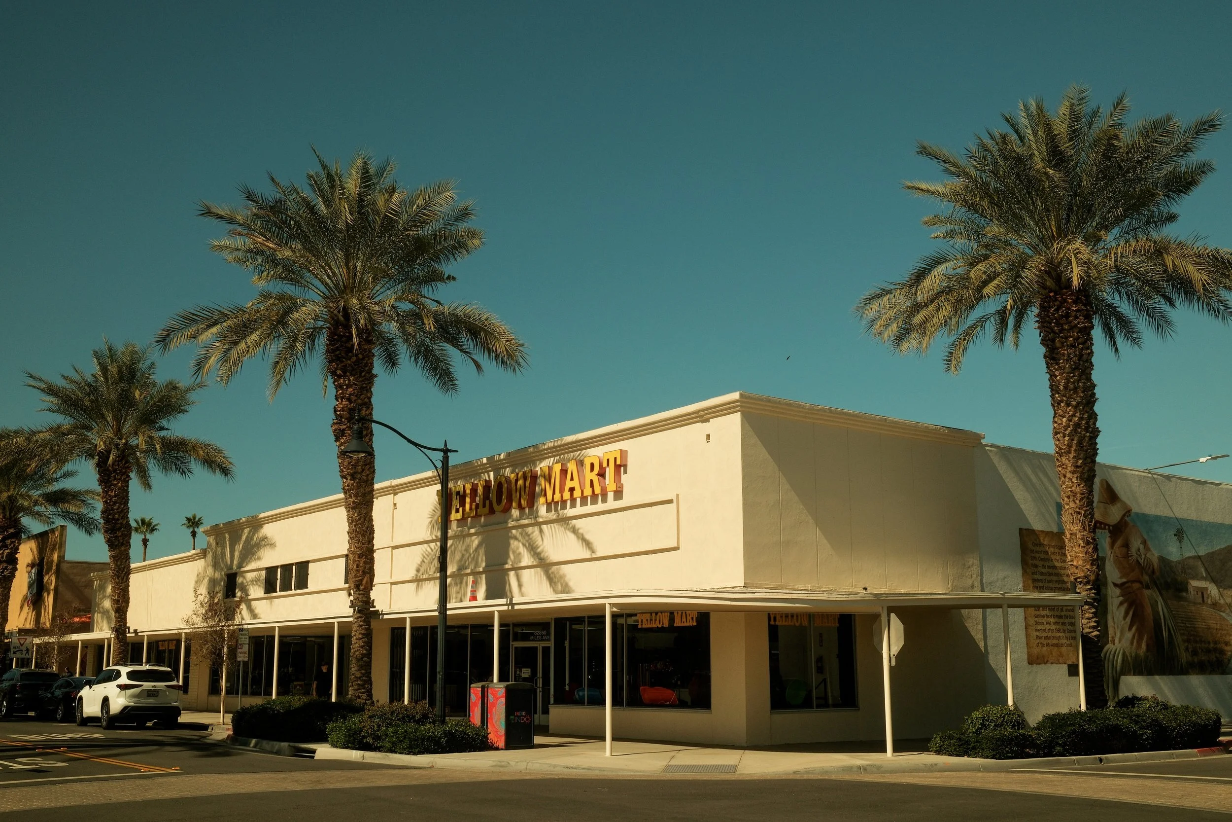 A shopping center with the sign 'Yellow Mart' on the front, surrounded by palm trees under a clear blue sky.