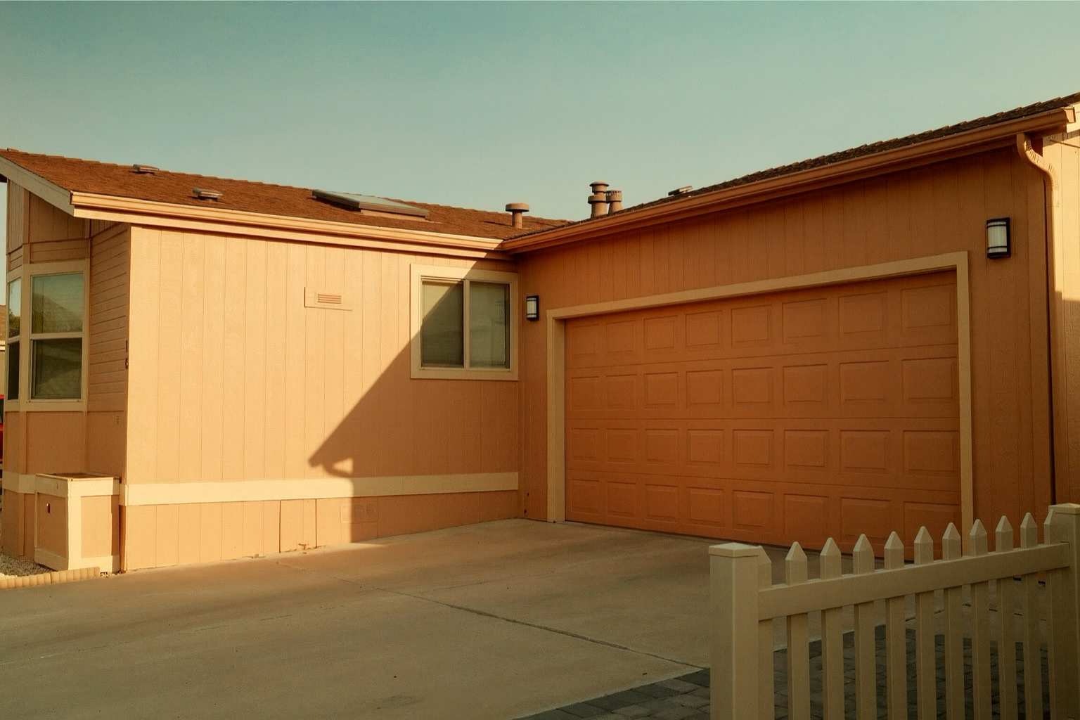 A peach-colored house with a garage, a small window, and a white picket fence in front.
