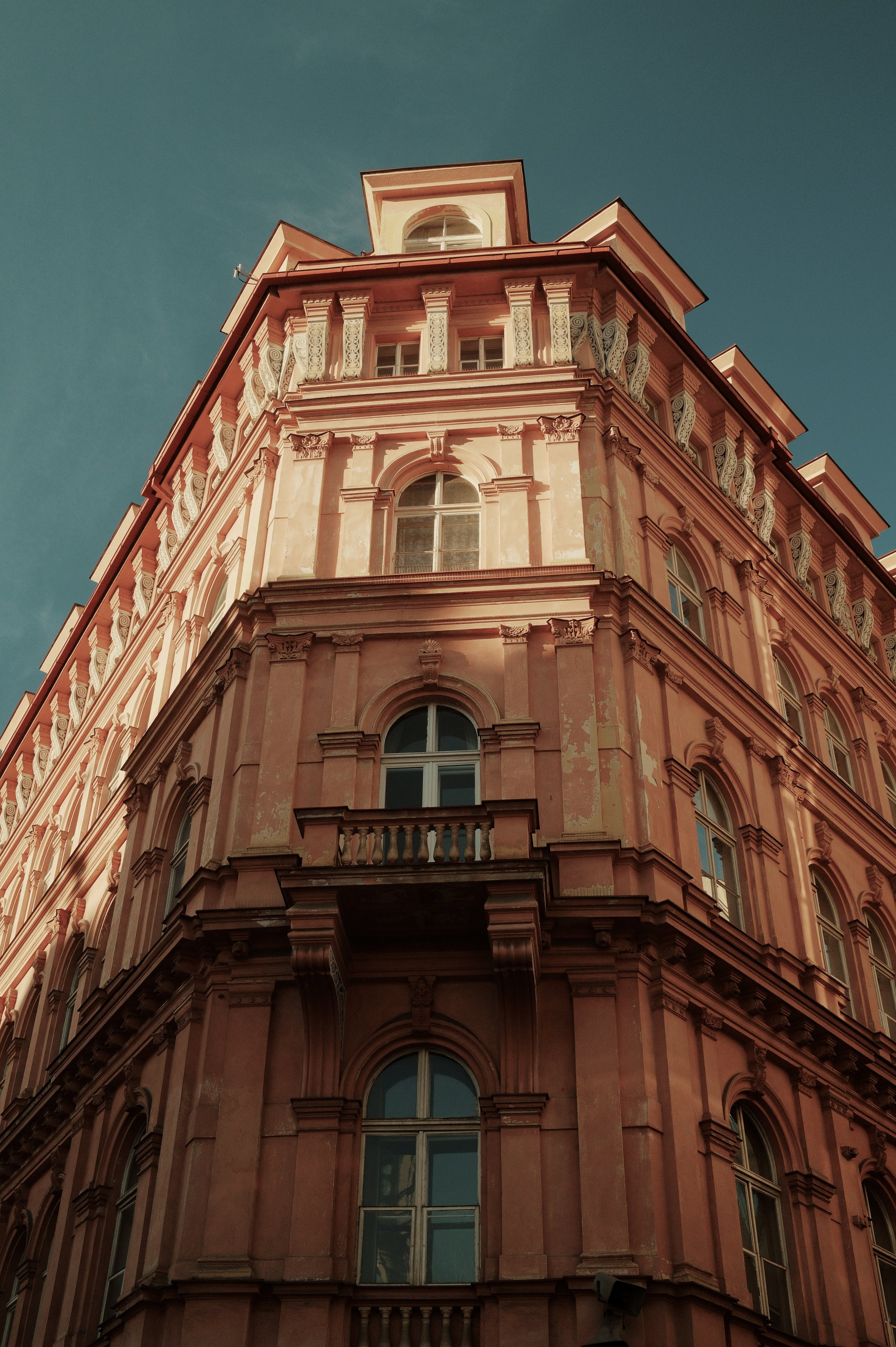 A tall, pink-colored historic building with ornate architectural details viewed from the ground looking upwards against a clear blue sky.