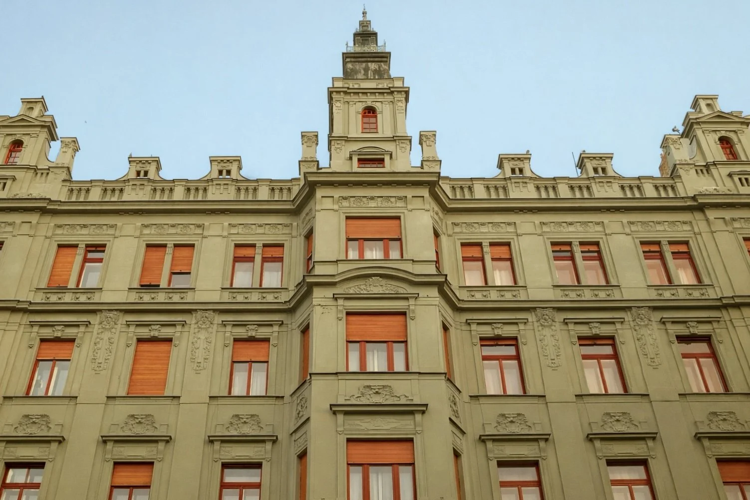 The facade of an ornate, historic building with multiple windows and decorative architectural details, topped with a tower against a clear blue sky.