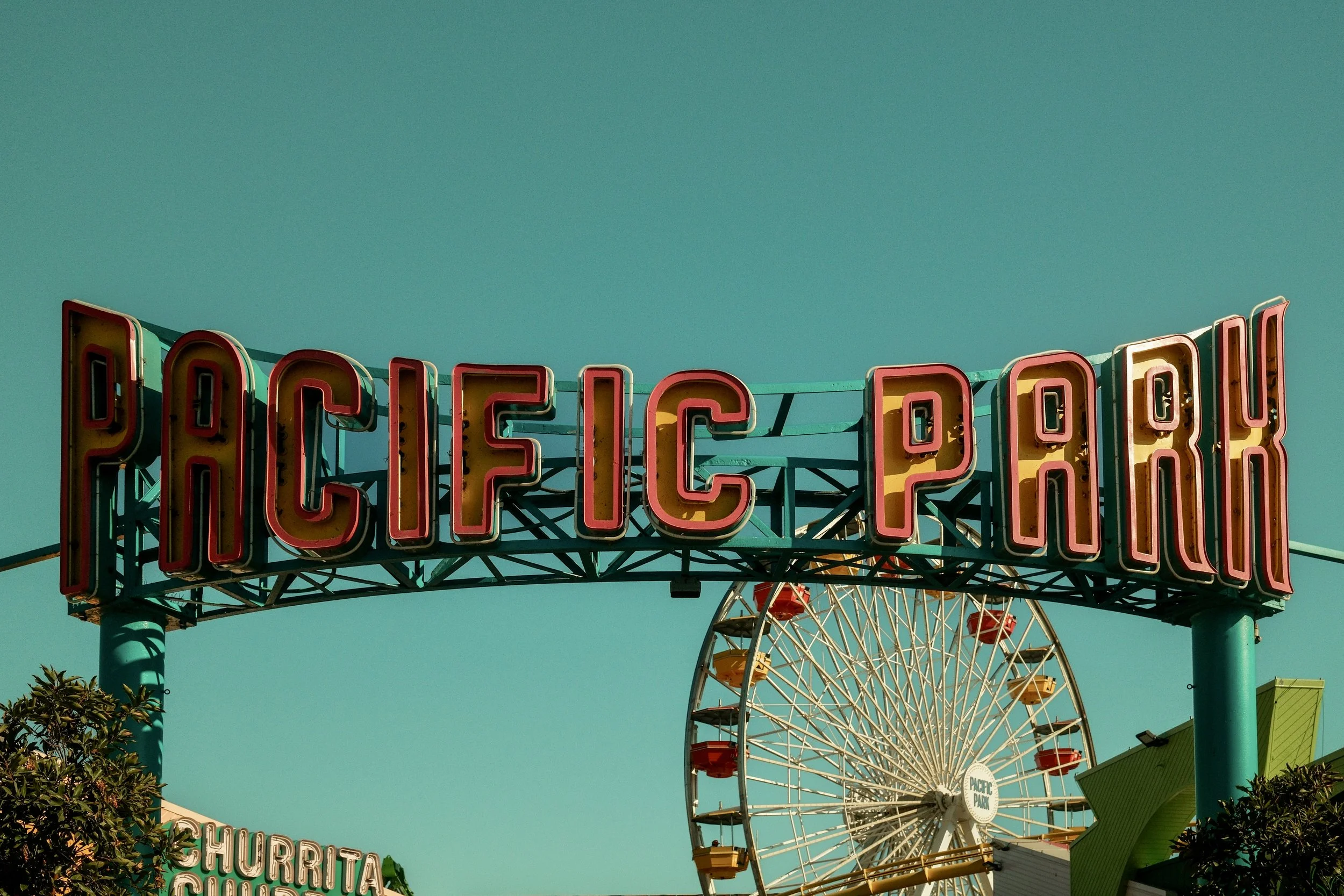 Vintage neon sign reading 'Pacific Park' with a Ferris wheel in the background on a clear day.