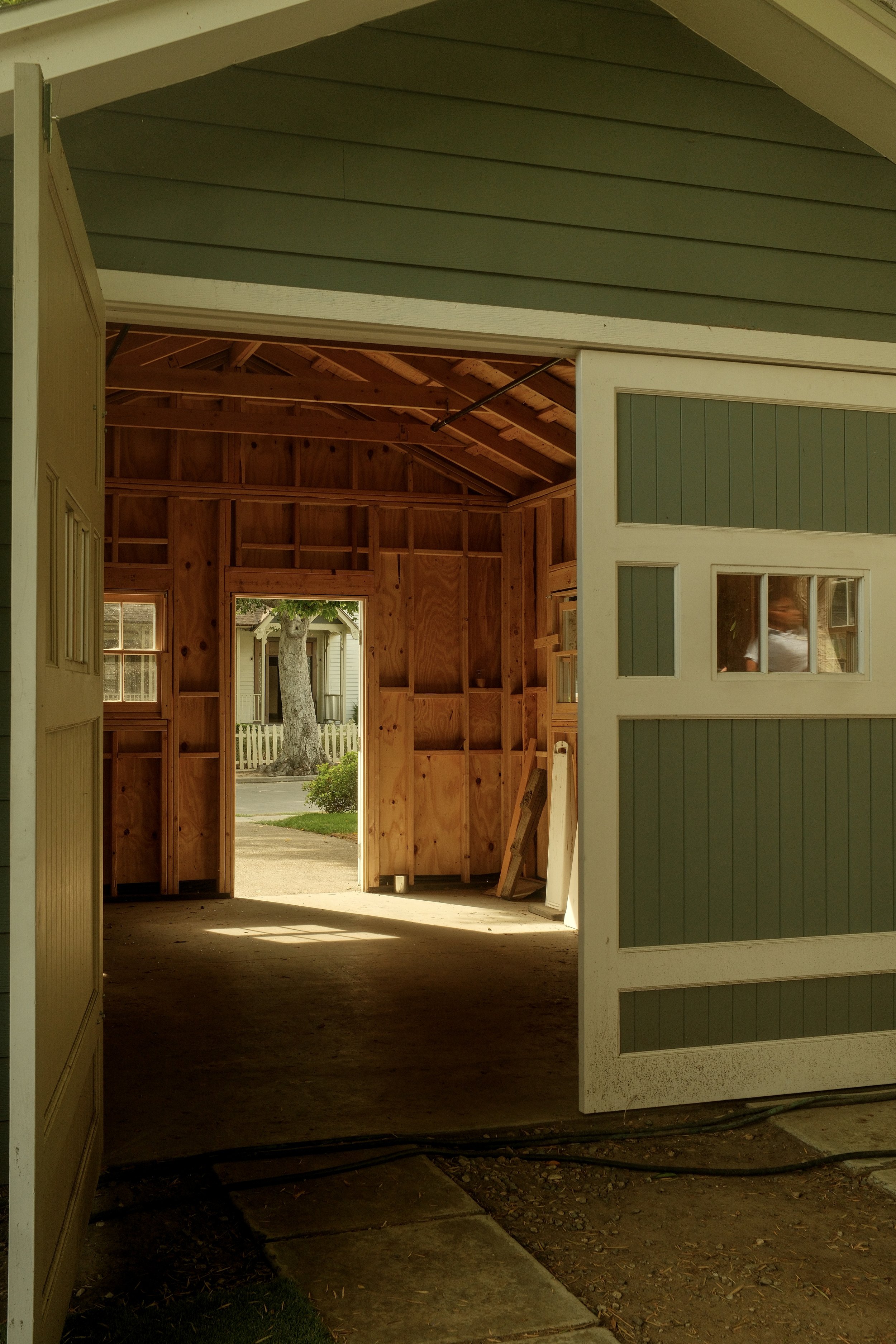 View inside an unfinished garage, showing exposed wooden framing and a partially installed sliding door, with a glimpse of the street and house across the road.