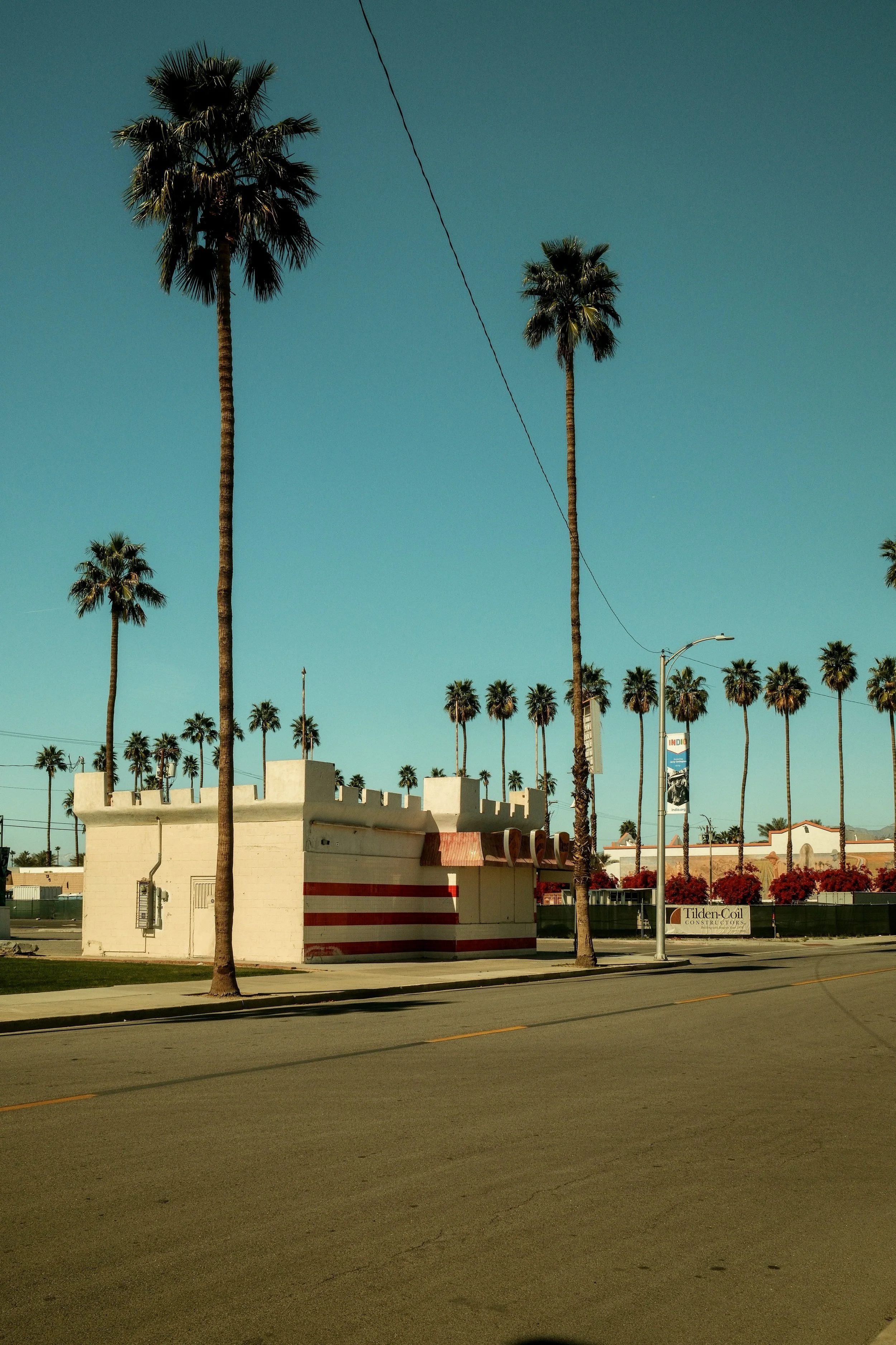 A street scene with tall palm trees lining the road and a white wall with red stripes resembling a castle tower.