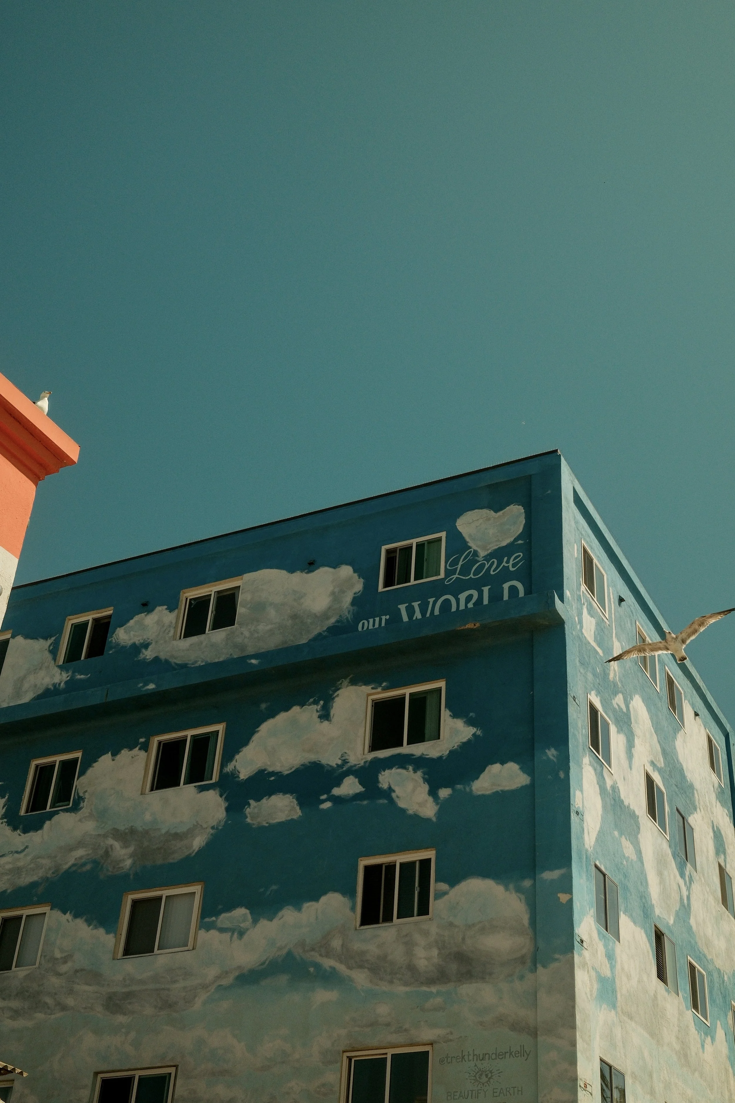 A building painted with a mural of blue sky and white clouds, featuring the words "Love our World" and a sky with a bird flying.