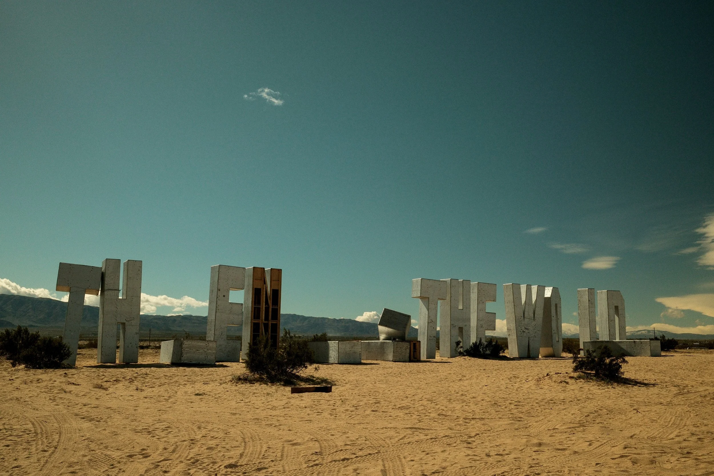 Large concrete letters spell out "THE TOWN" in a desert landscape with mountains and a blue sky in the background.