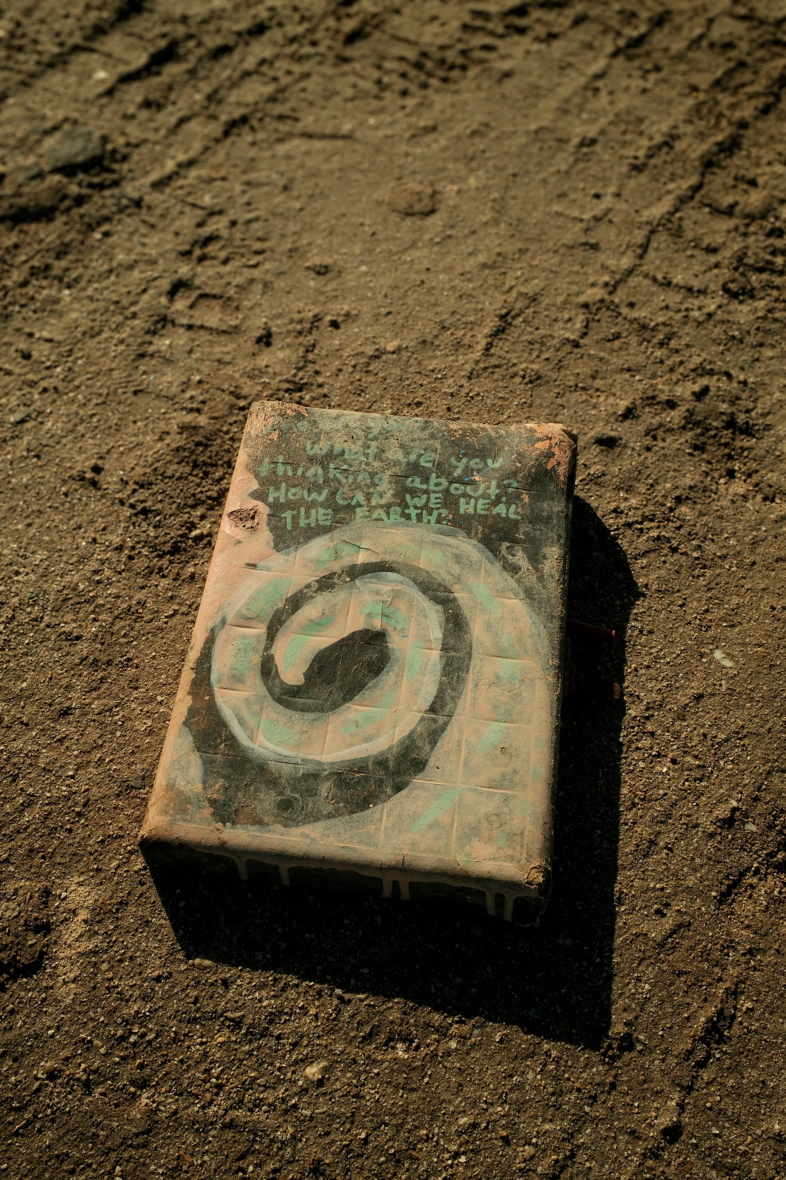 A painted brick with a large number nine and a handwritten message on top, on a dirt surface.