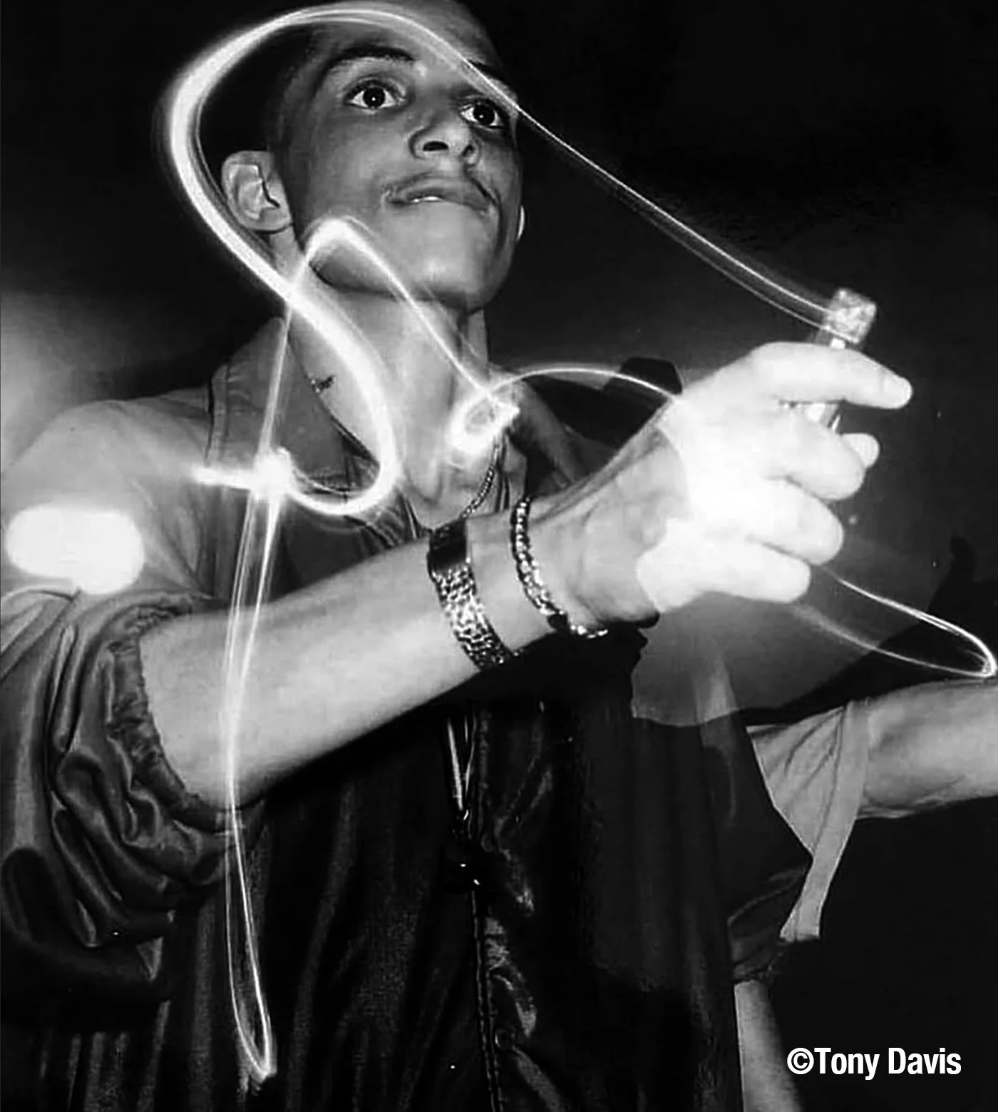 A young man in a leather jacket holding a cigarette, with light trails around him, in black and white. Credits to Tony Davis.