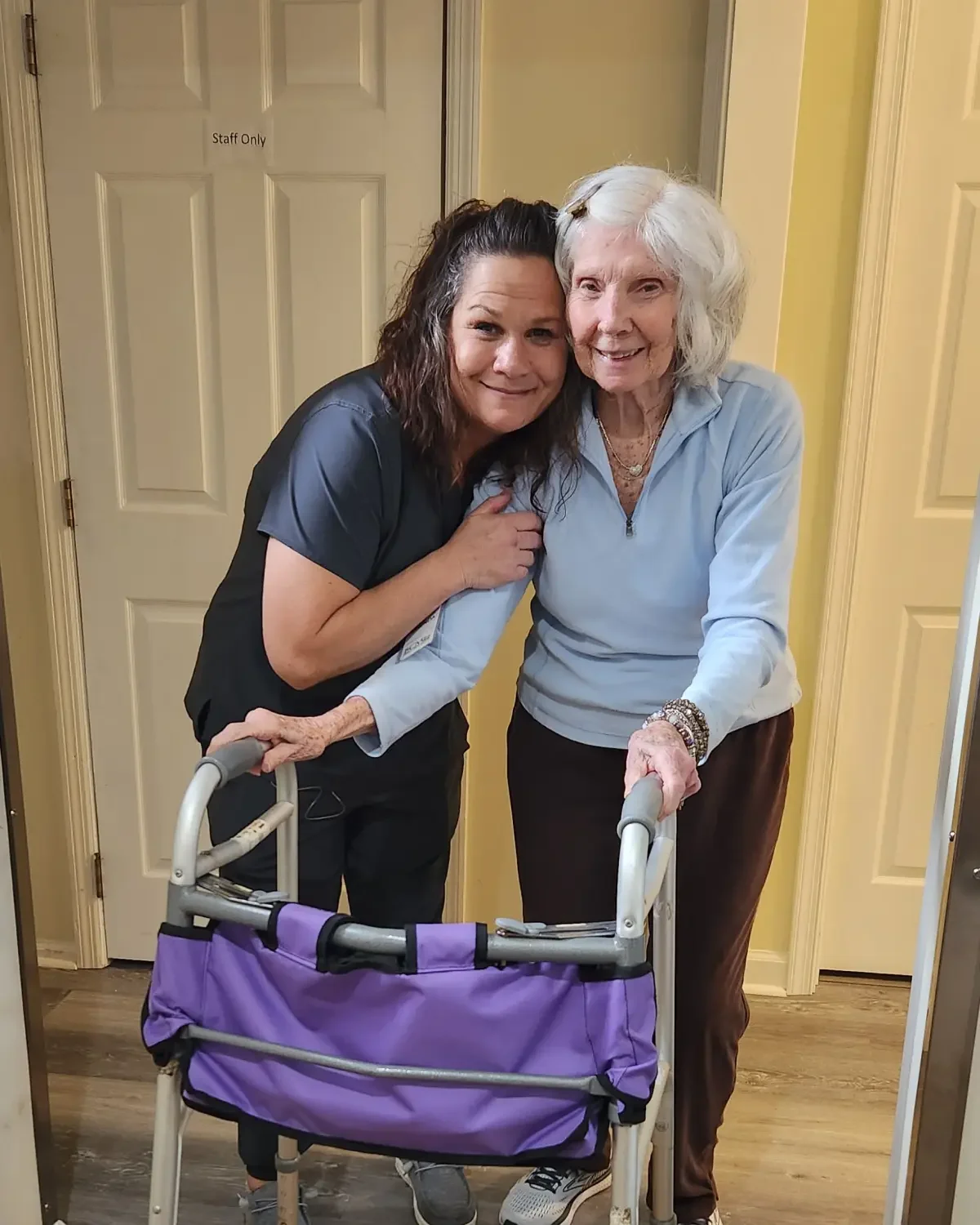 Caregiver warmly hugging a resident in the hallway at Broad Creek Manor, showing close relationships.