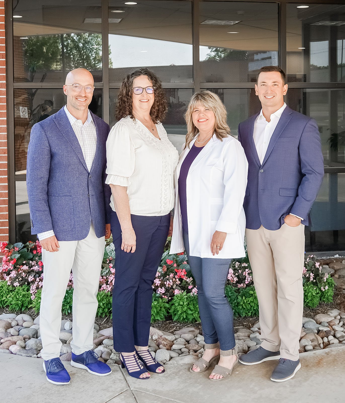 Four people, two men and two women, standing outside a building with glass windows, smiling at the camera.