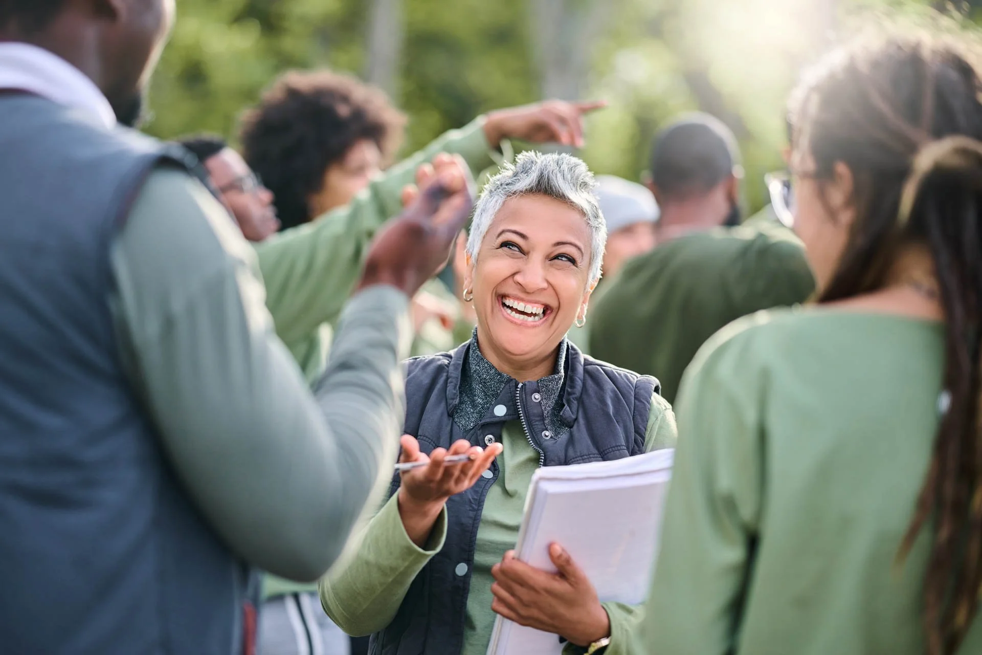 A smiling woman with short gray hair talking to a group of people outdoors.
