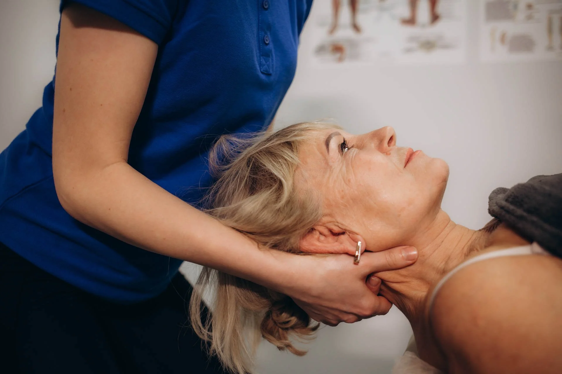 A healthcare professional performs a neck adjustment on a woman lying on her back in a medical setting.